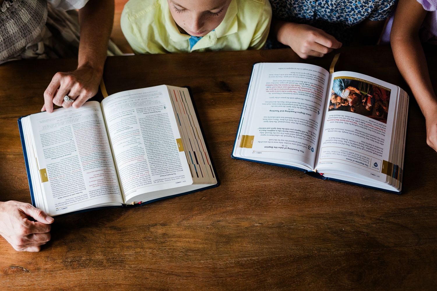 Adults and child reading open books together at a wooden table, studying religious texts in a family setting.