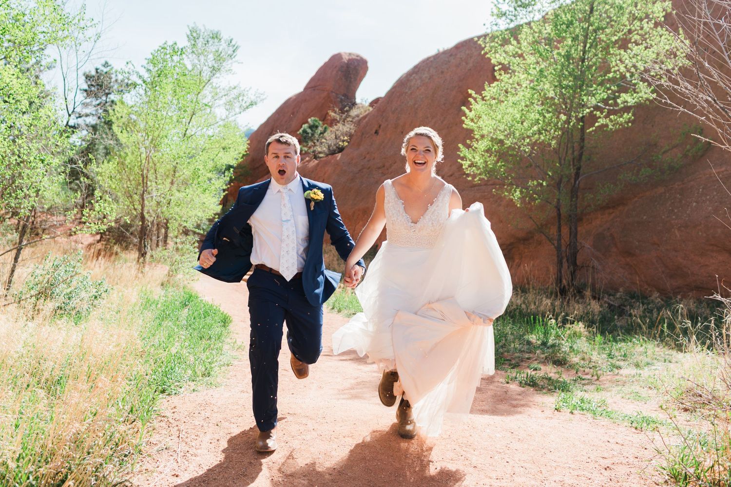 Joyful newlyweds run hand-in-hand through red rock formations in a stunning outdoor wedding photo.