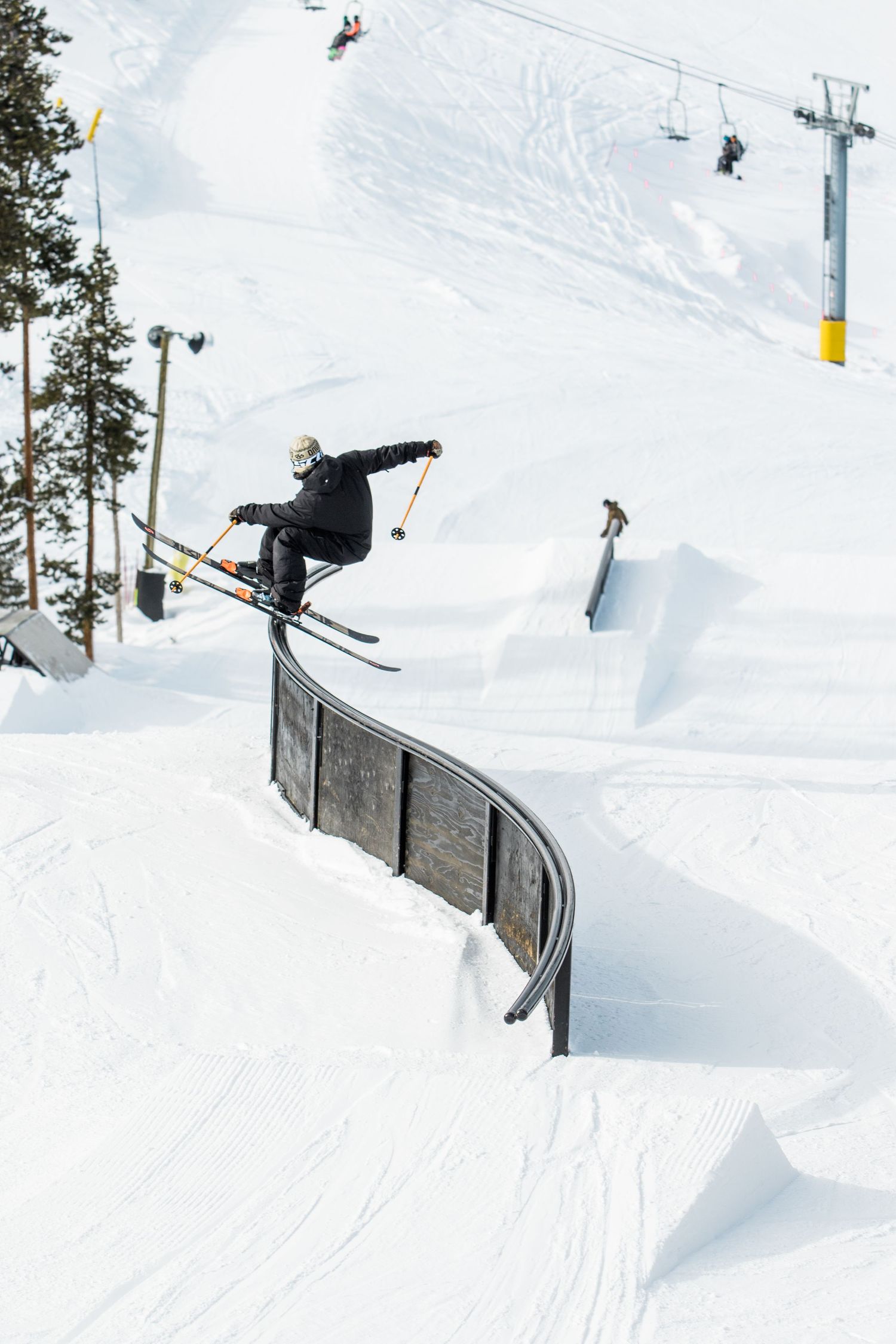 Skier performing a trick over a curved metal rail in a snow terrain park.