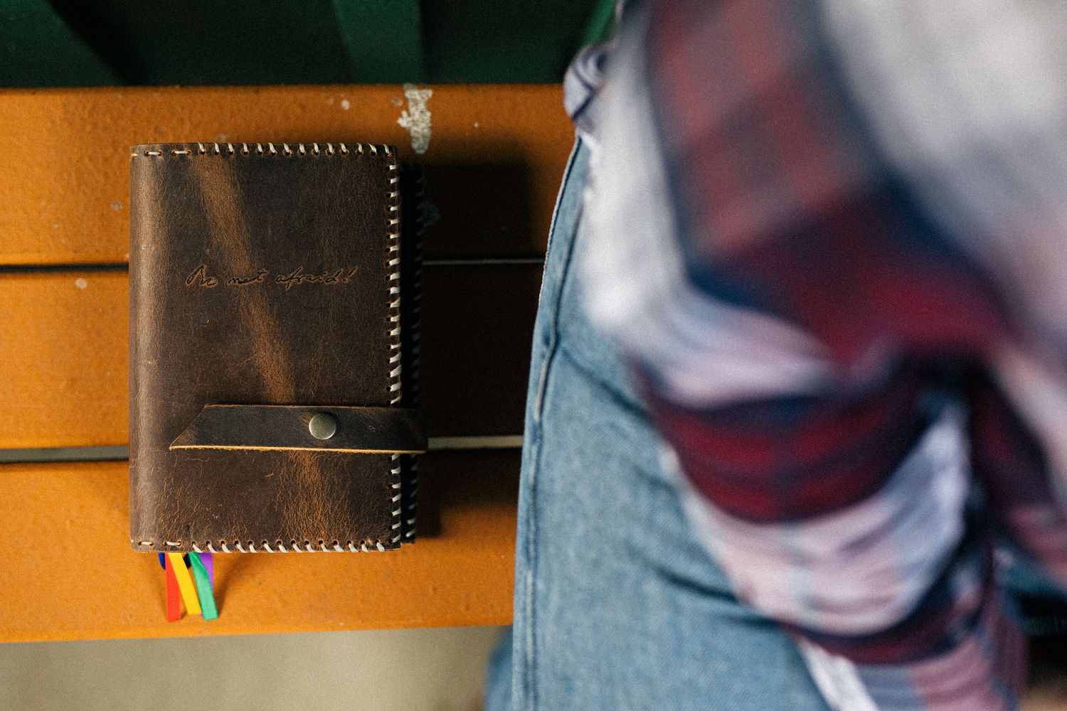 Close-up view of a brown leather wallet sitting on an orange surface next to someone wearing blue jeans.