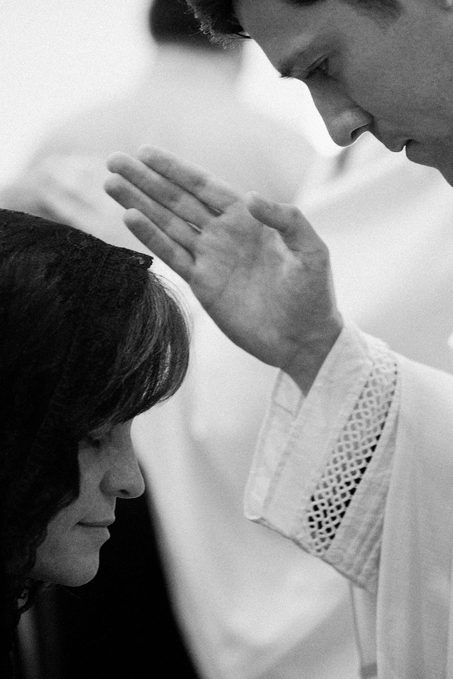Black and white photo of a priest blessing a woman with raised hand during a religious ceremony.