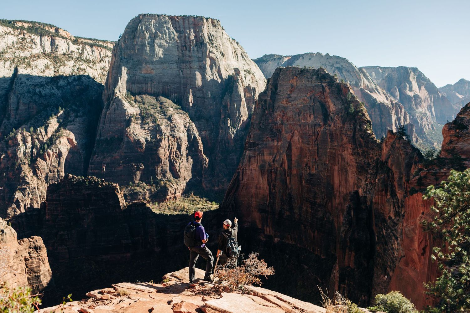 Hikers stand atop Angels Landing summit overlooking the dramatic red rock canyons of Zion National Park in Utah.