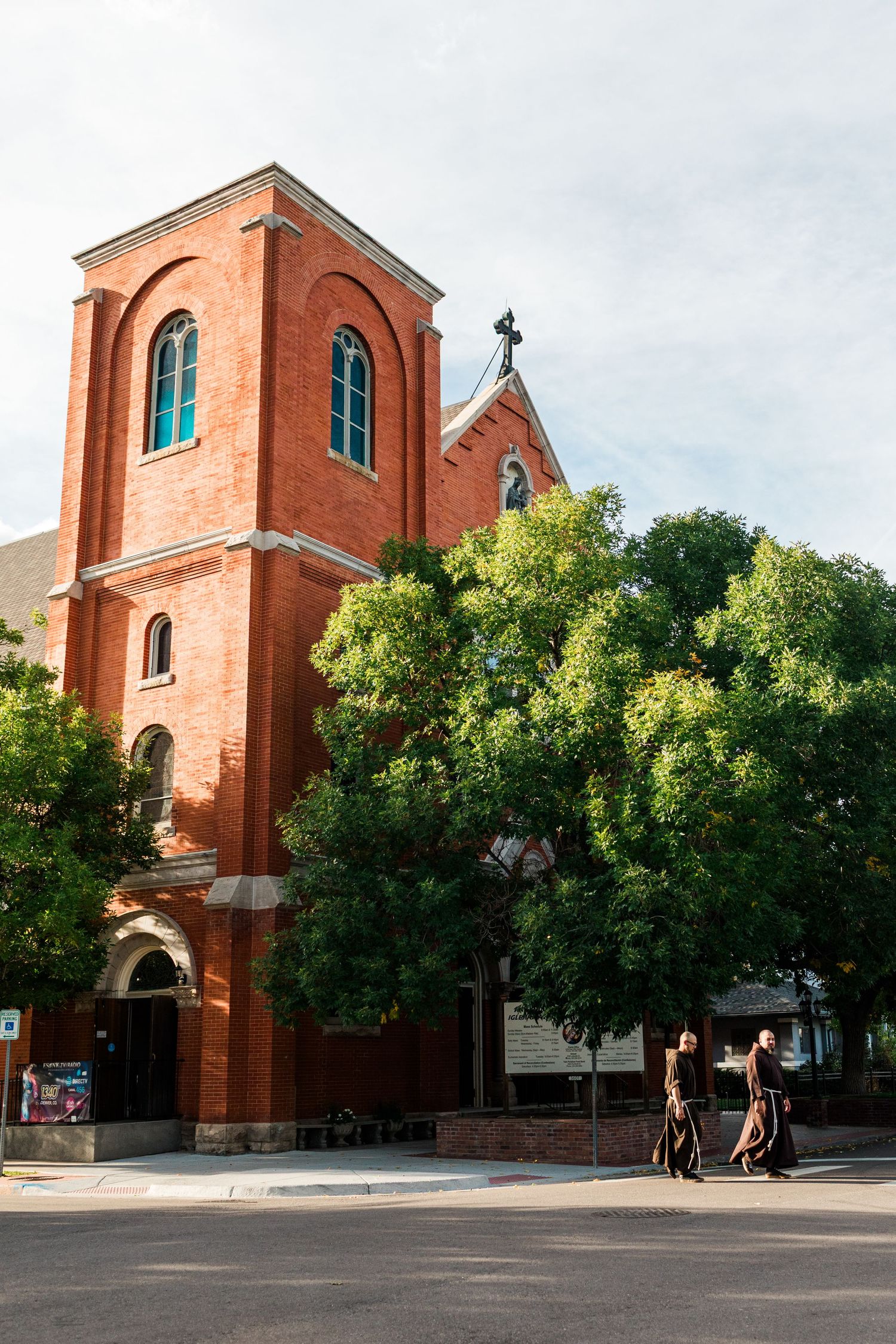 Red brick church exterior with Gothic architecture features and green trees lining the sidewalk.
