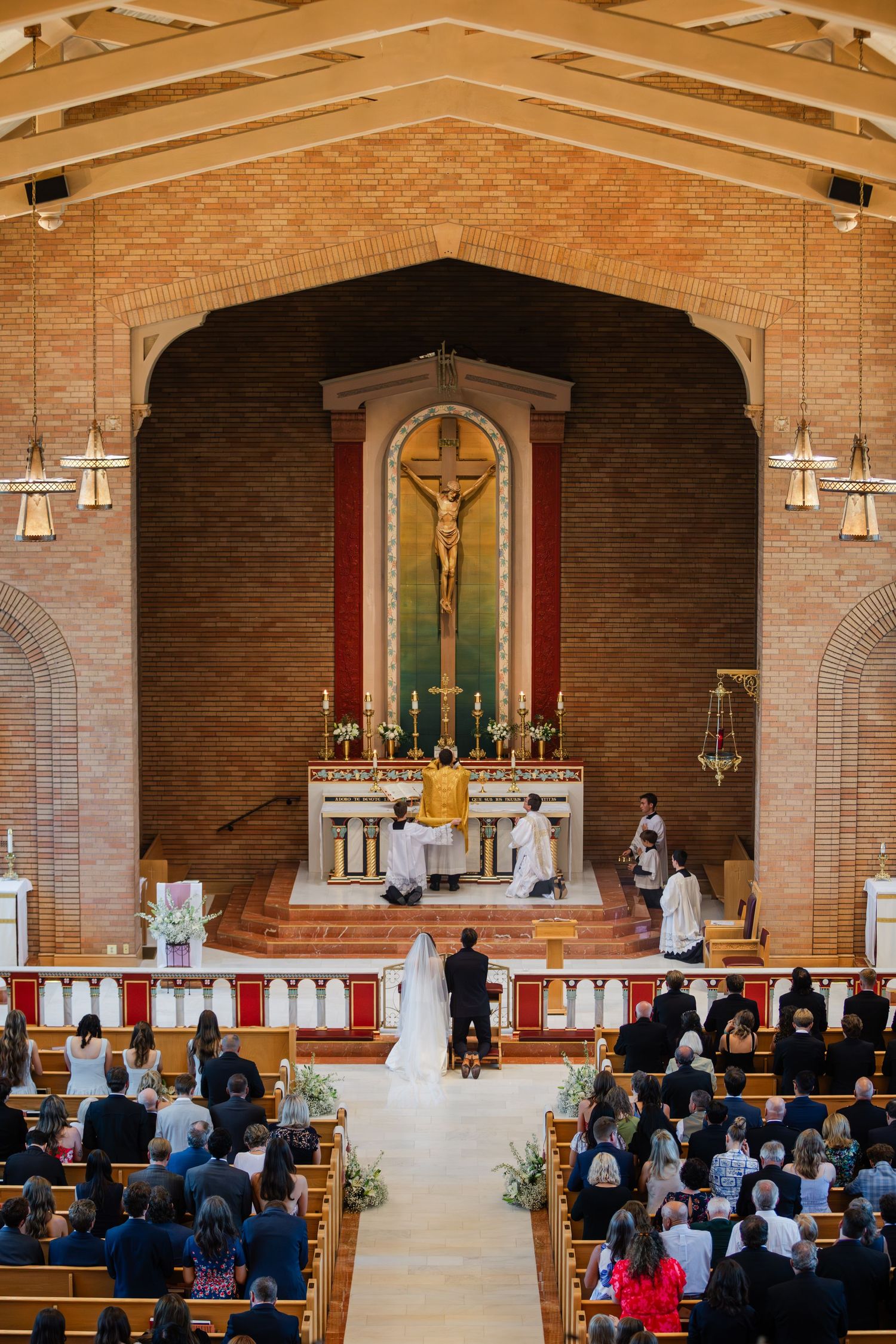 A Catholic wedding ceremony progresses through different moments in a brick church with guests seated in wooden pews.