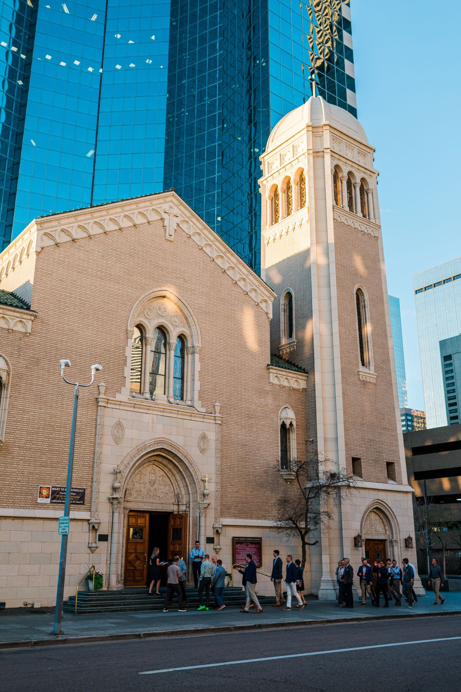 Historic stone church with bell tower stands beside modern glass skyscrapers on a sunny urban street.