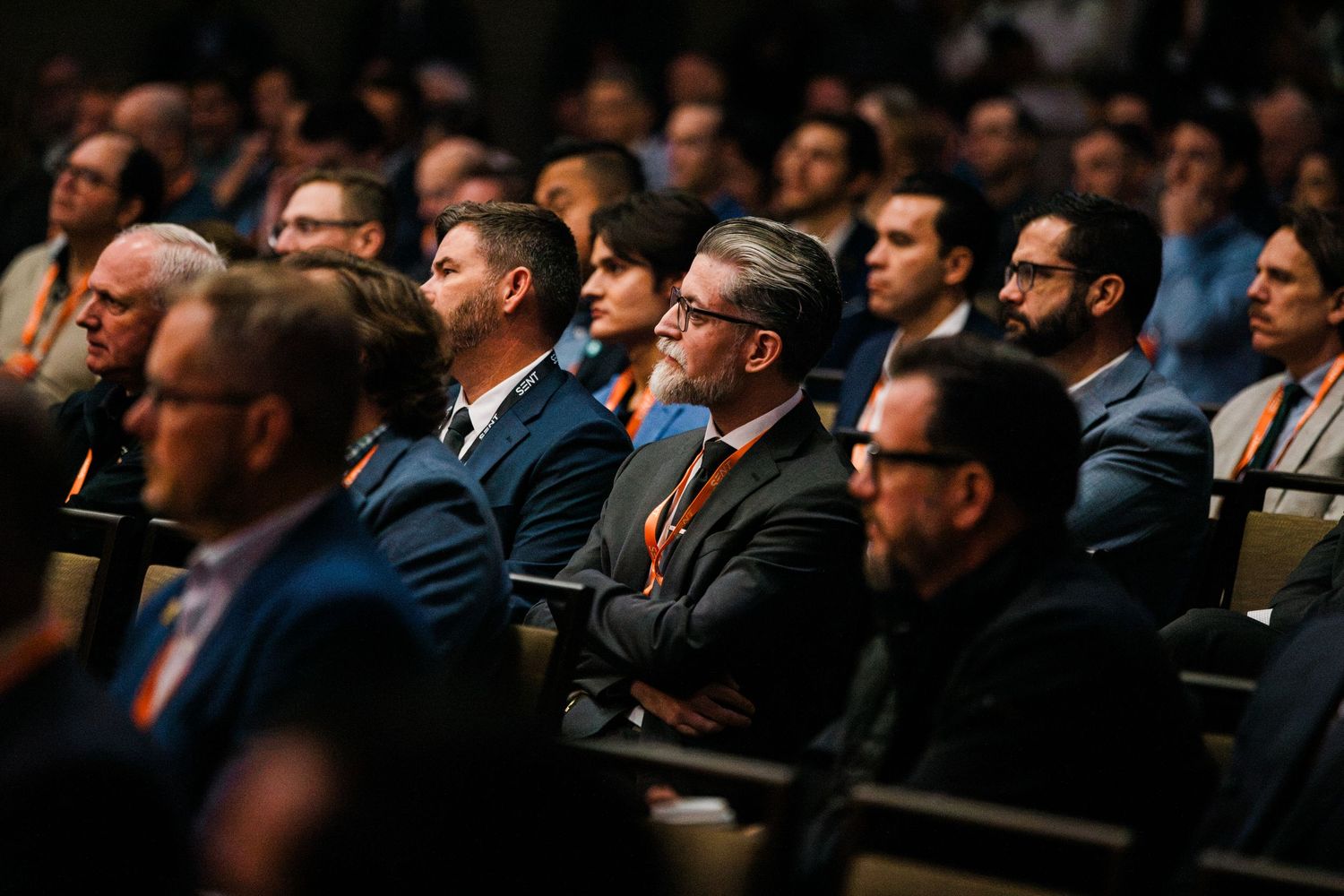 Audience of business professionals in suits attentively watching a presentation at a corporate conference event.