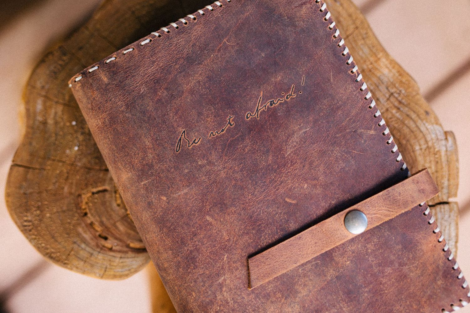 A handcrafted brown leather wallet with white stitching rests on a rustic wooden surface showing beautiful patina.