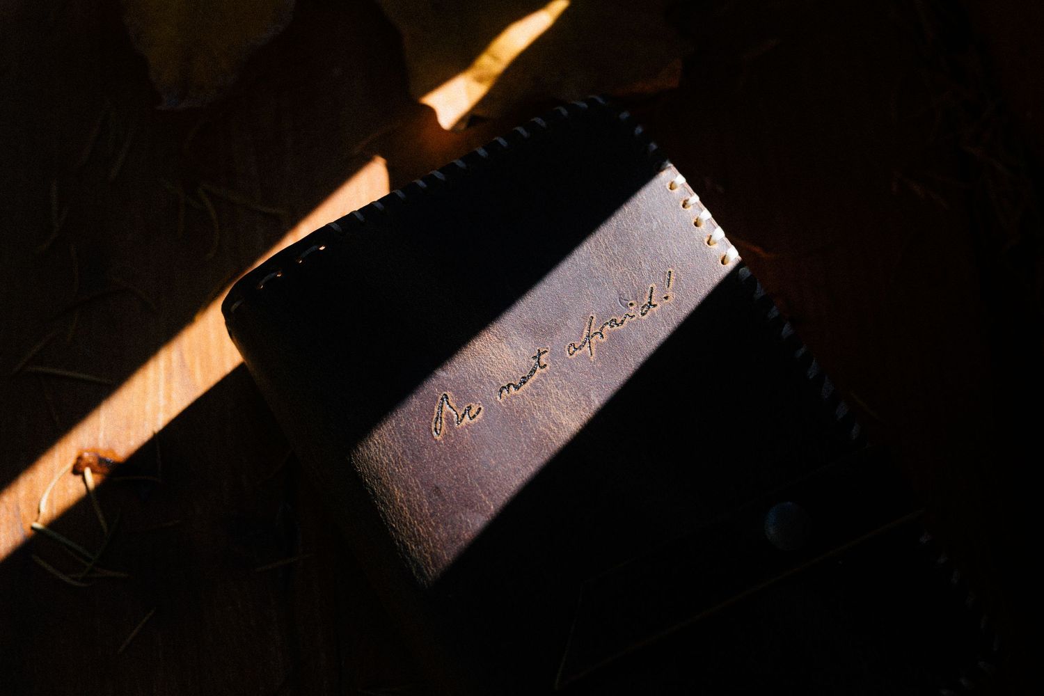 A calligraphy pen writing on brown paper with dramatic side lighting creating strong shadows.