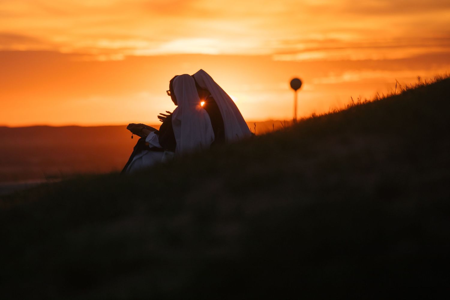 Silhouette against dramatic orange sunset sky over rolling hills.