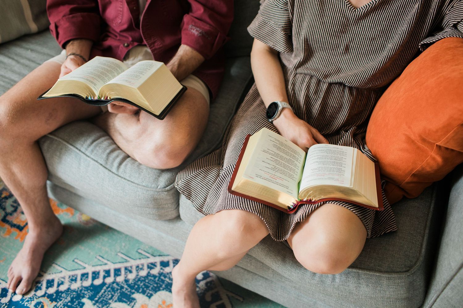 Two people sitting on a couch reading open Bibles together in a casual home setting.
