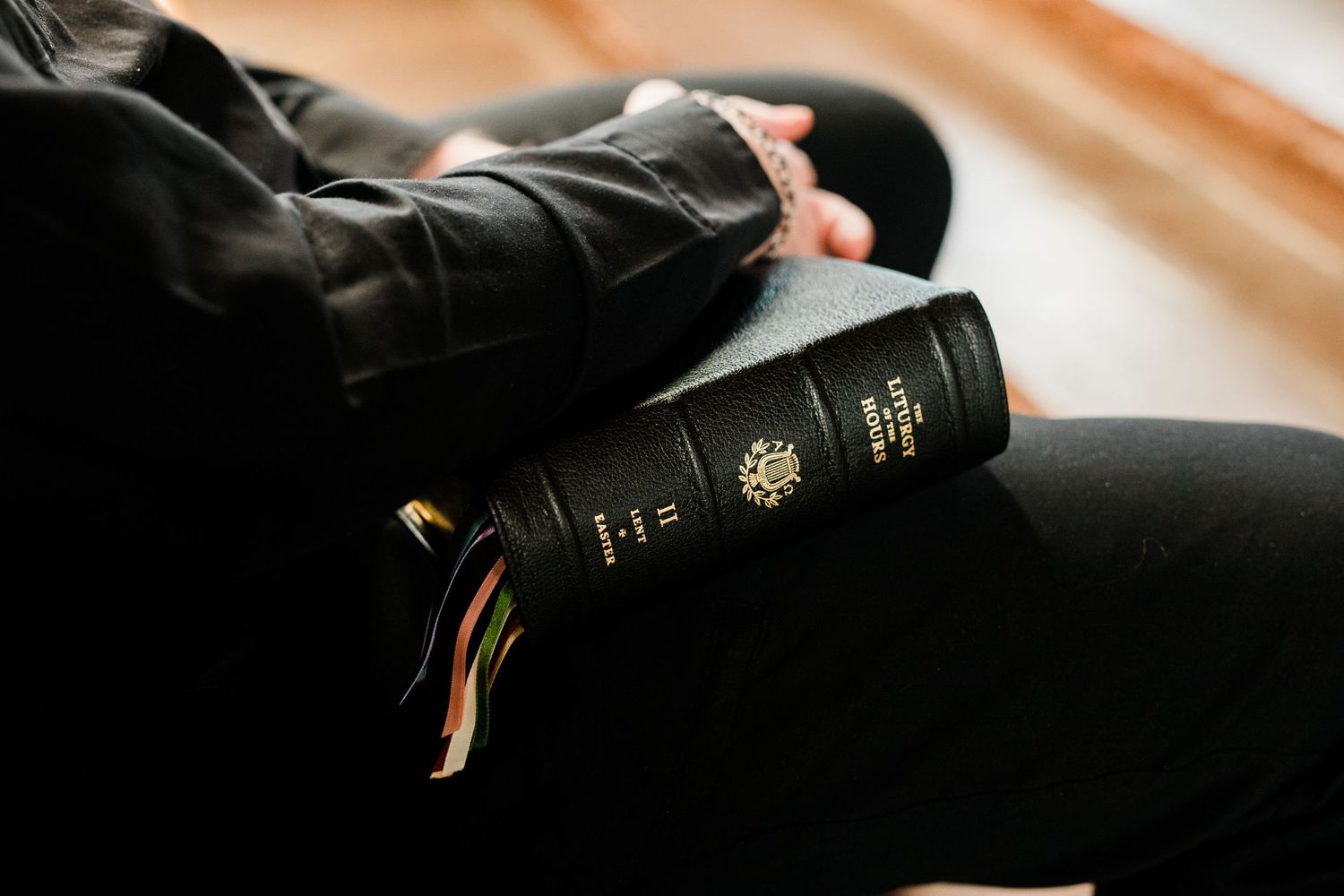 Person holding a black Holy Bible on their lap while seated, with colorful ribbon bookmarks visible.