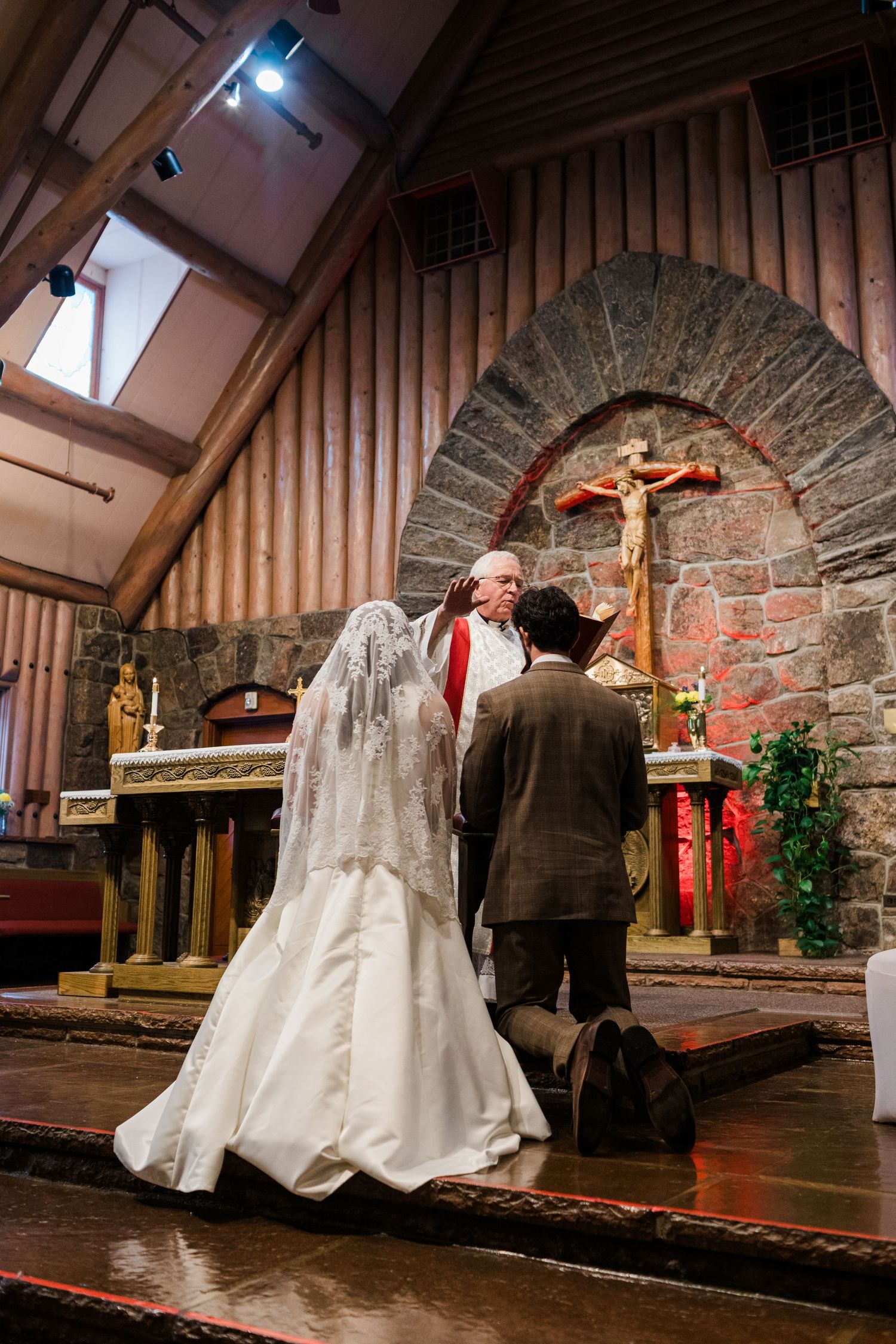Bride and groom kneeling at altar during Catholic wedding ceremony in a stone church with crucifix.