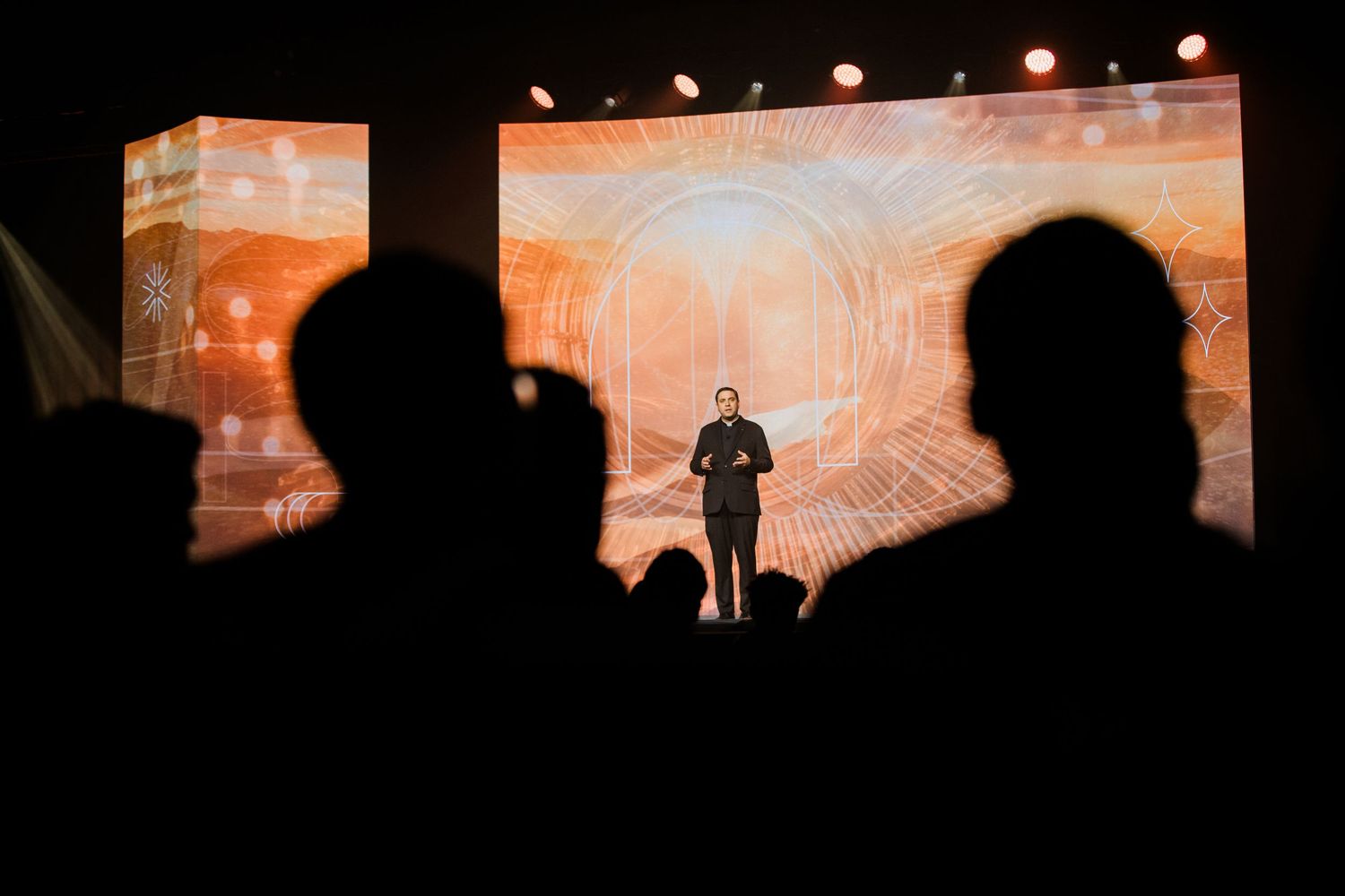 Silhouettes of performers on stage against an orange and white backdrop during a theatrical production.