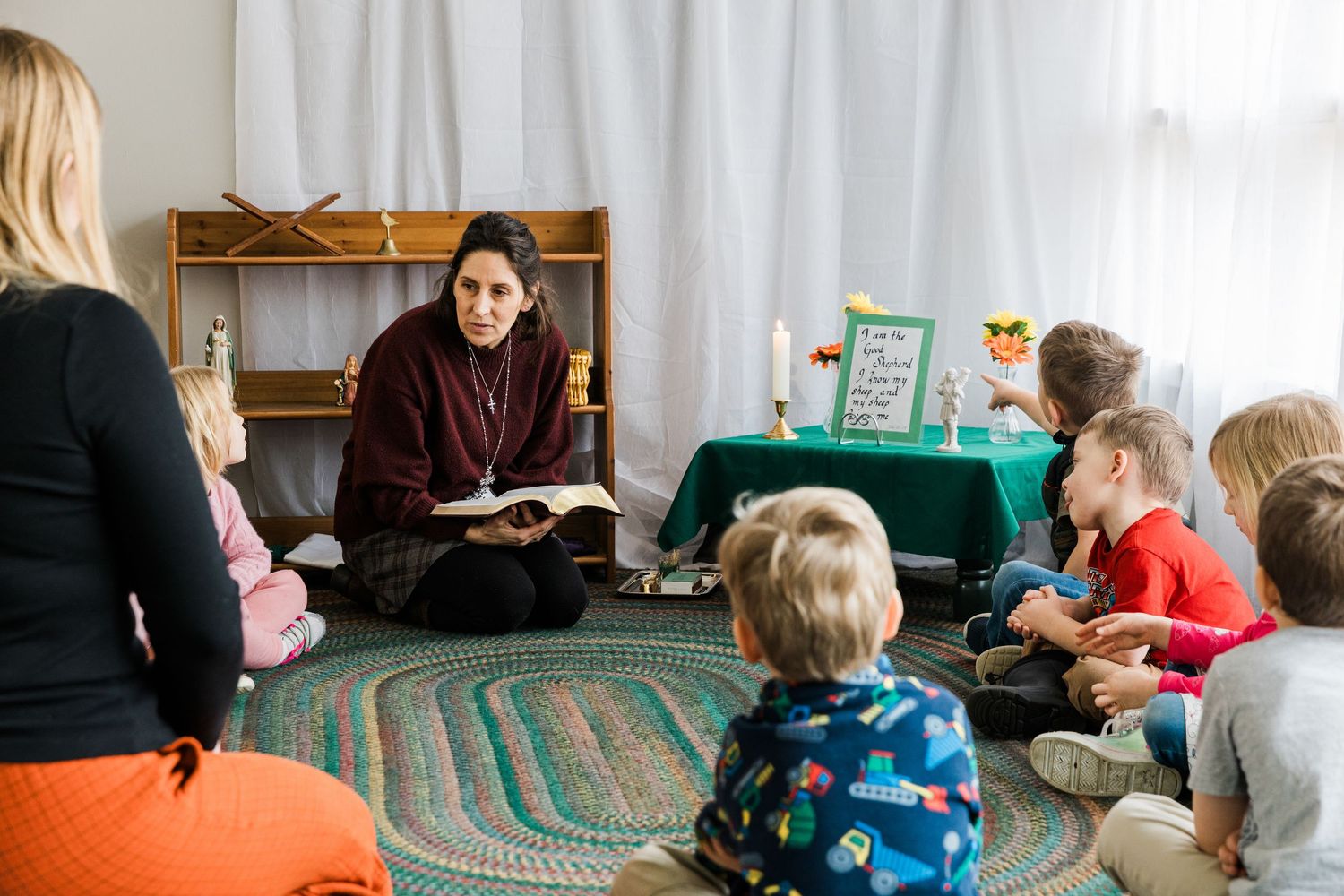 Child and caregiver read a book together while lying on a blue-colored carpet on the floor.