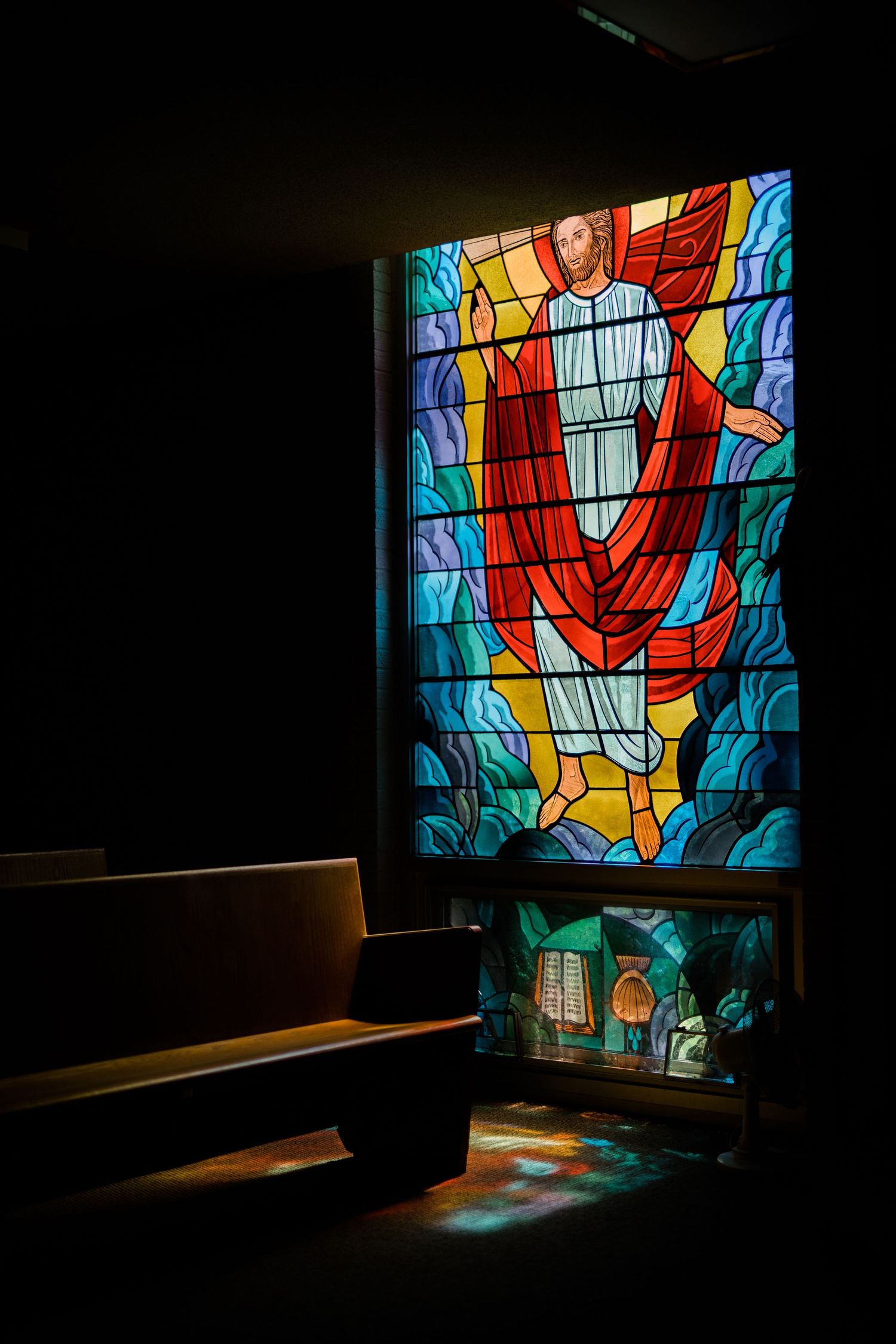 Colorful stained glass window in a church casting vibrant light onto wooden pews.