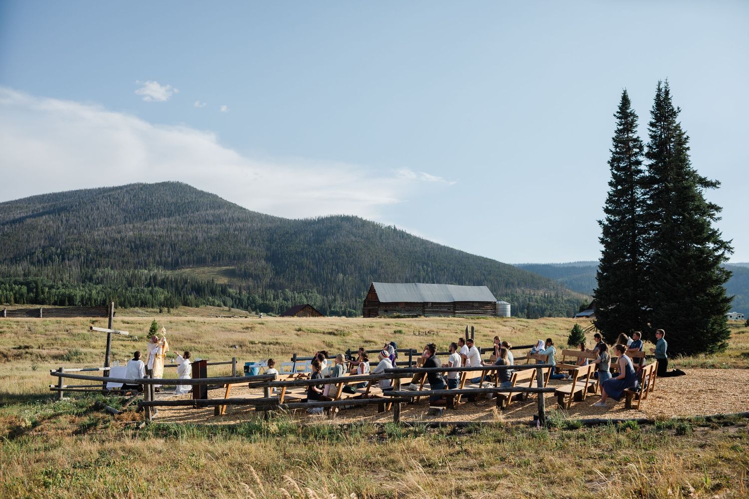 A scenic mountain landscape with evergreen trees and a gathering of people in an outdoor setting.