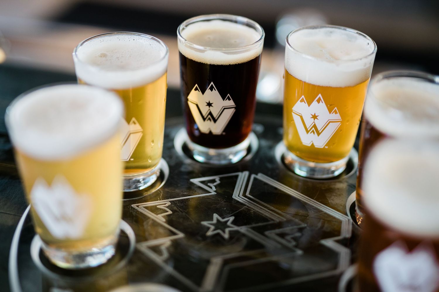 Multiple glasses of craft beer lined up on dark surface showing variety of beer styles.