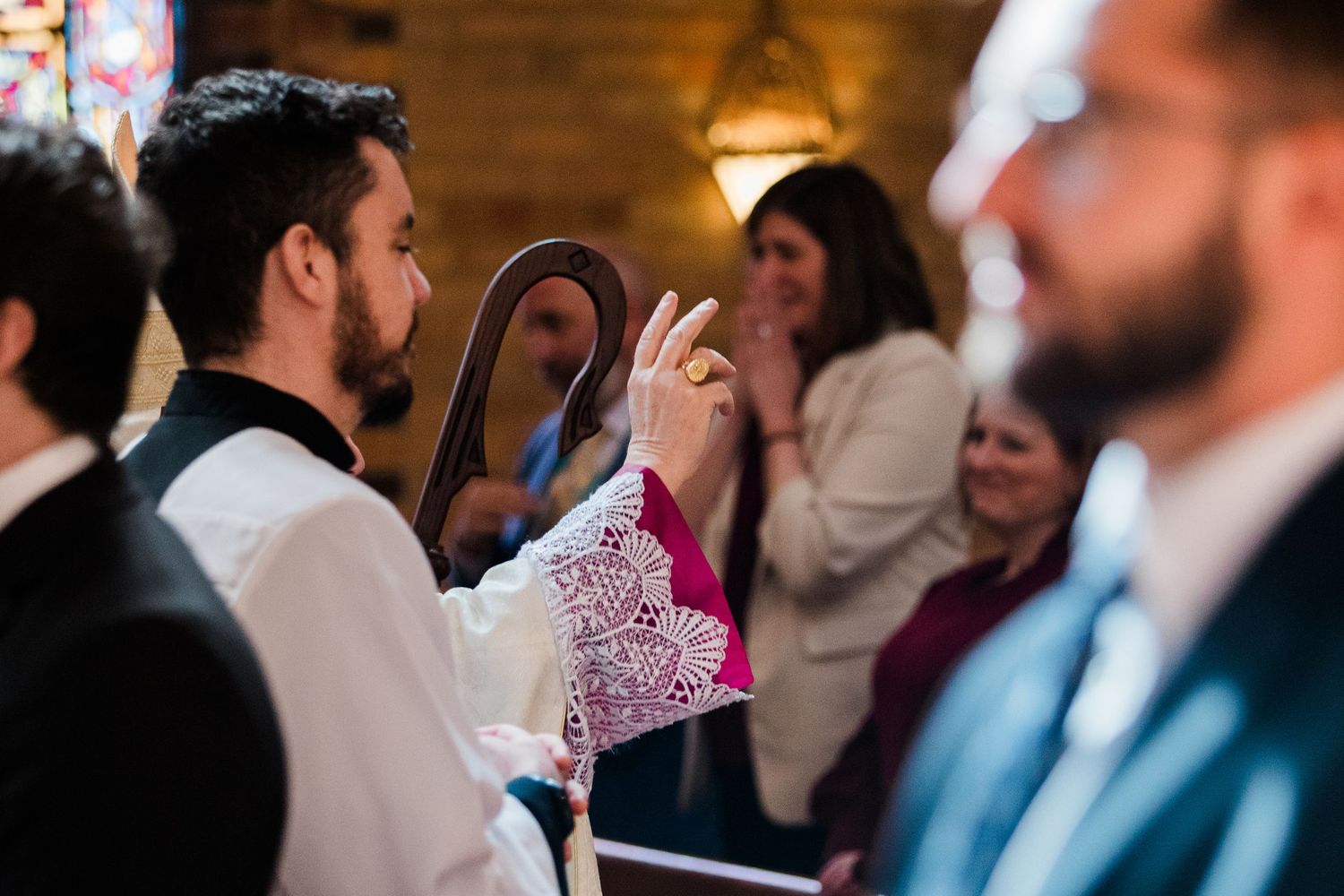 Priest giving a blessing during a wedding ceremony inside a church with guests in the background.