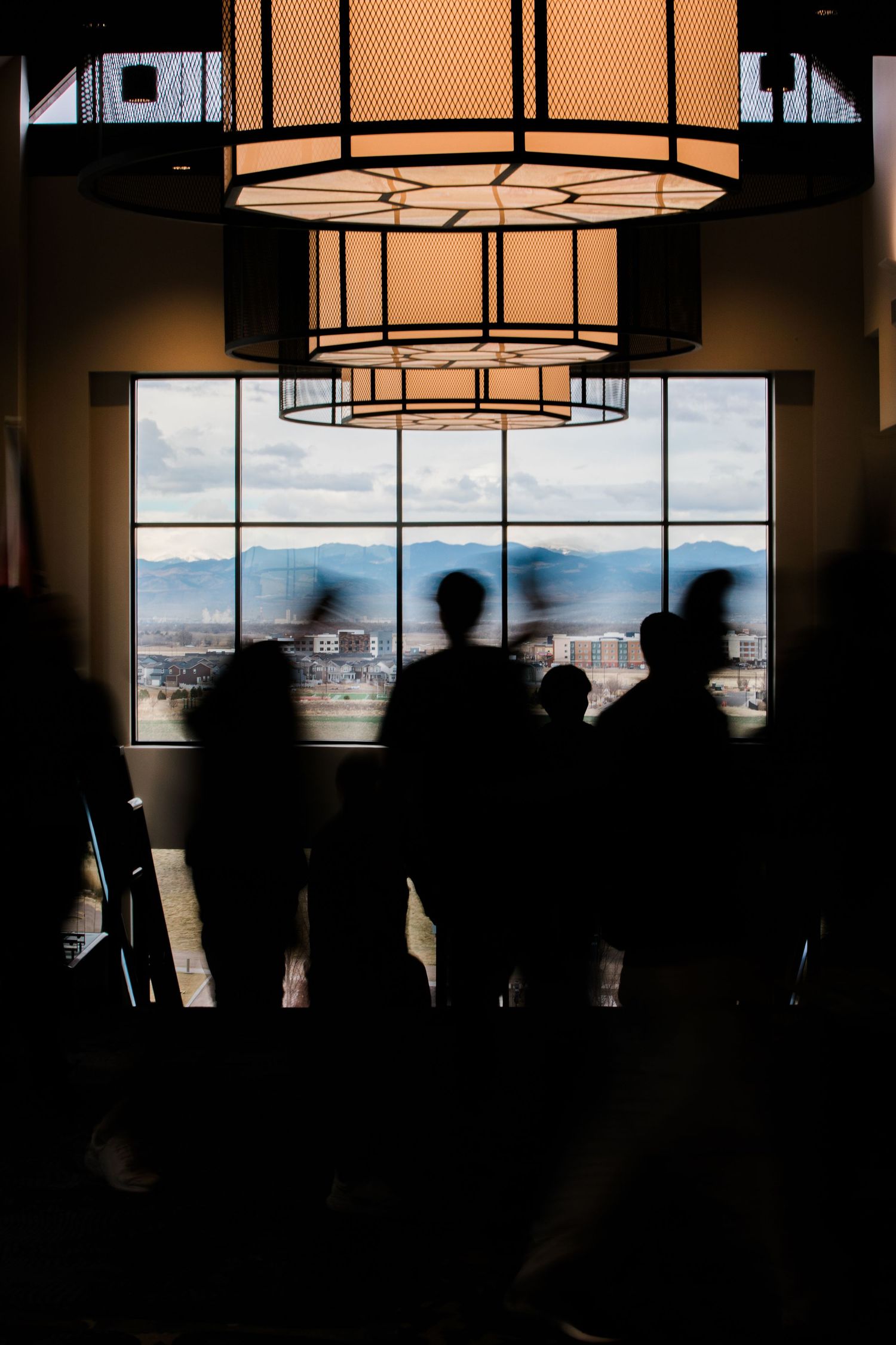 Silhouettes of people standing against large windows with modern pendant lights hanging in a contemporary interior space.