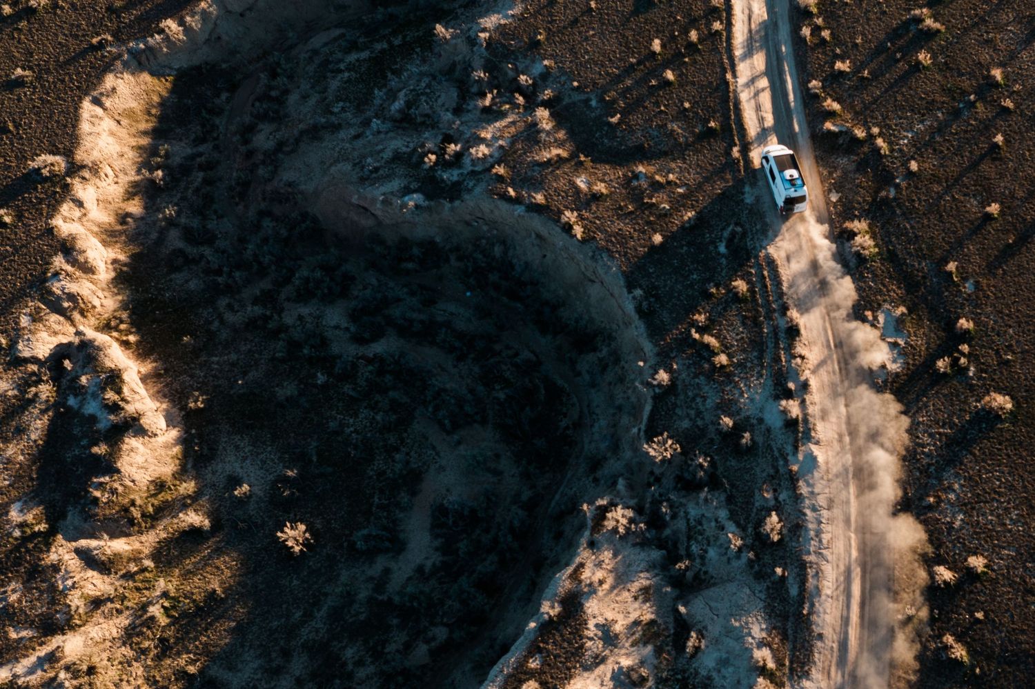 Aerial view of a winding mountain road cutting through snowy terrain and dark forest landscape at sunset.