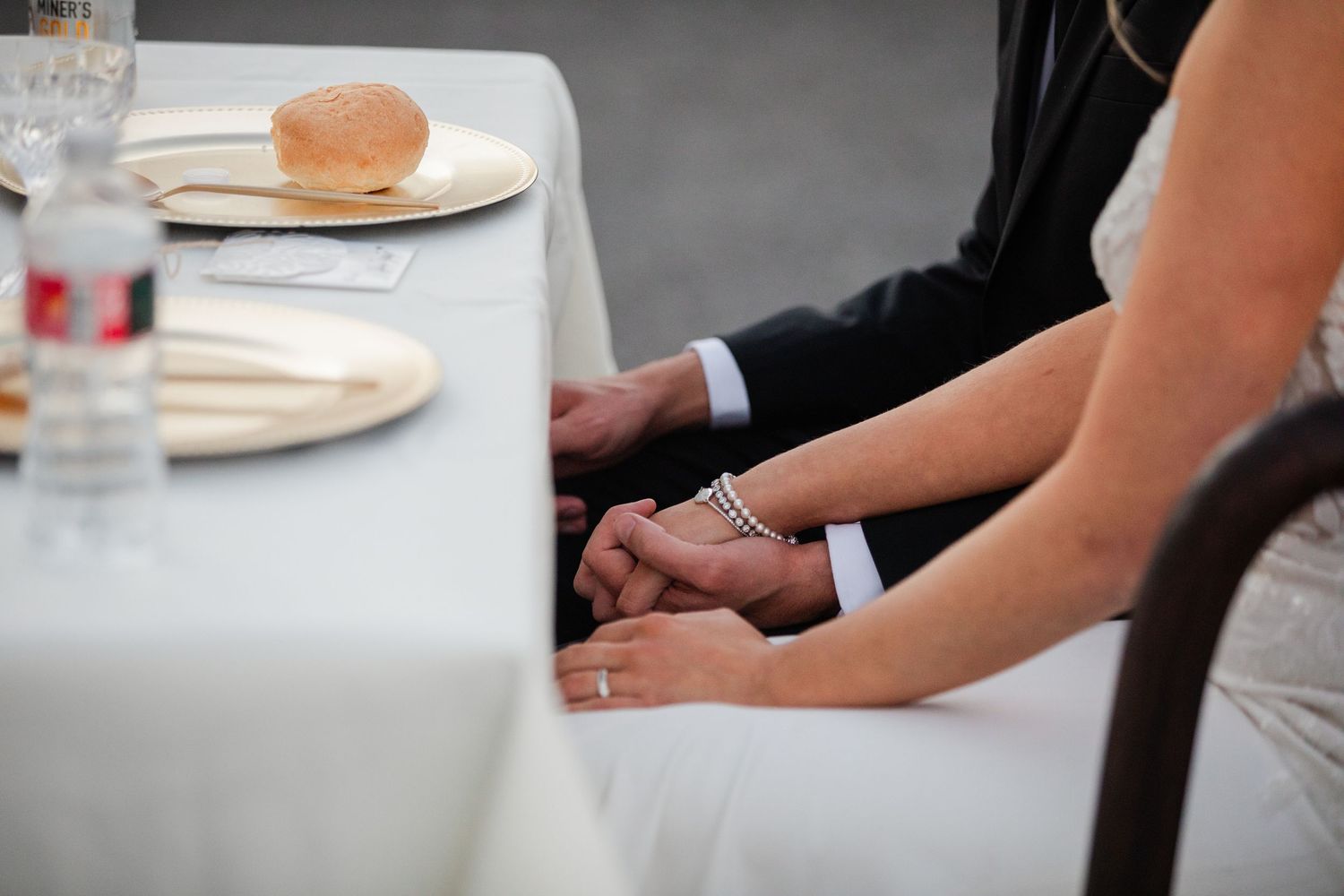 Bride and groom holding hands at wedding reception table with bread rolls and place settings.