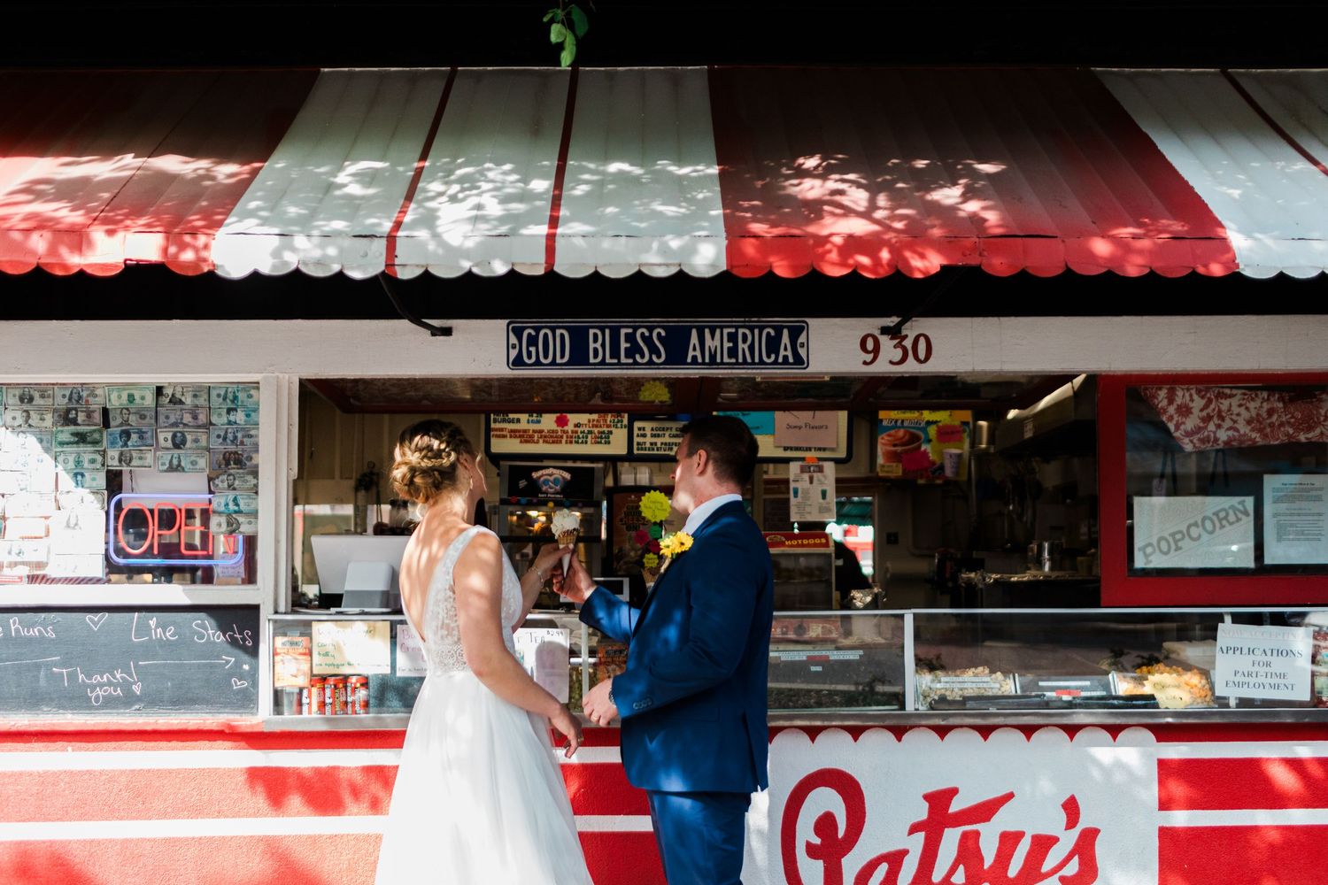 Bride and groom sharing a romantic moment at Patsy's food stand with a God Bless America sign backdrop.