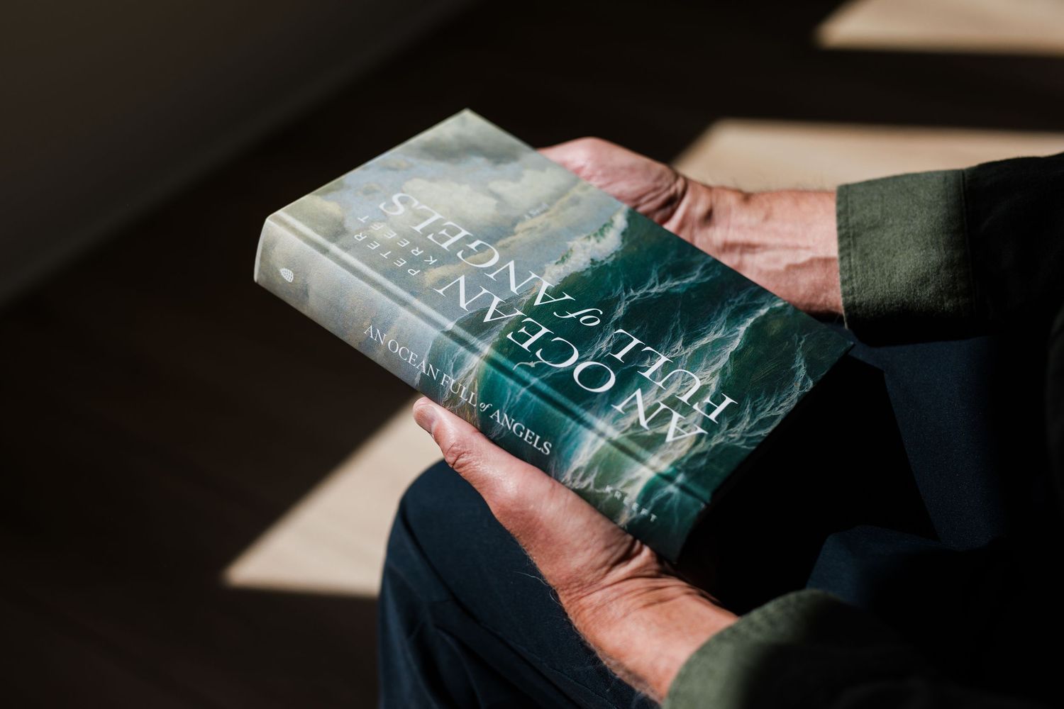 Elderly hands holding a hardcover book titled An Ocean of Minutes by Thea Lim in natural sunlight.