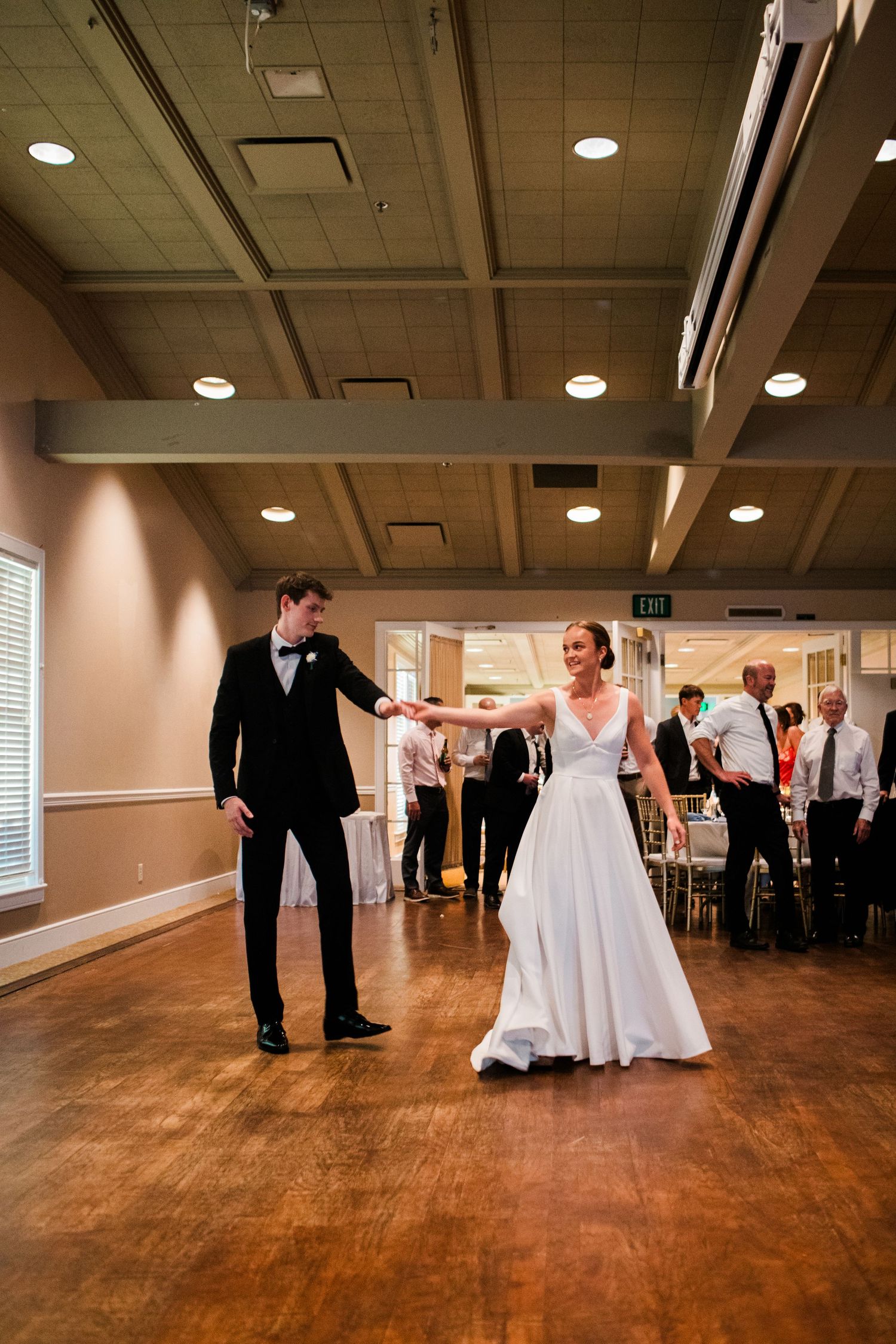 Bride and groom share joyful first dance on wooden floor at elegant wedding reception venue.
