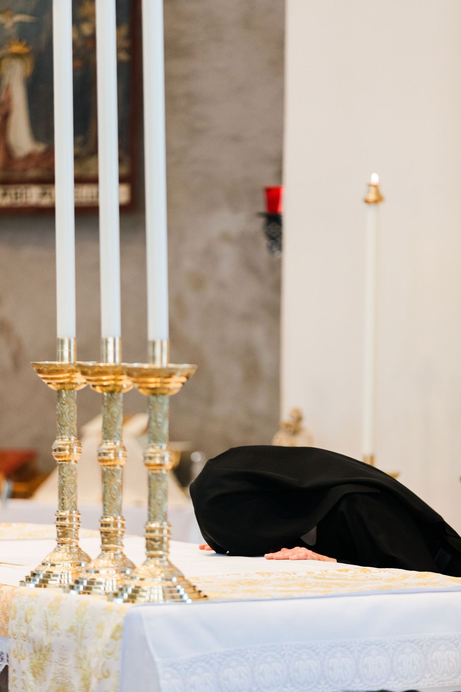 Priest prostrating at church altar with golden candlesticks during religious ceremony.