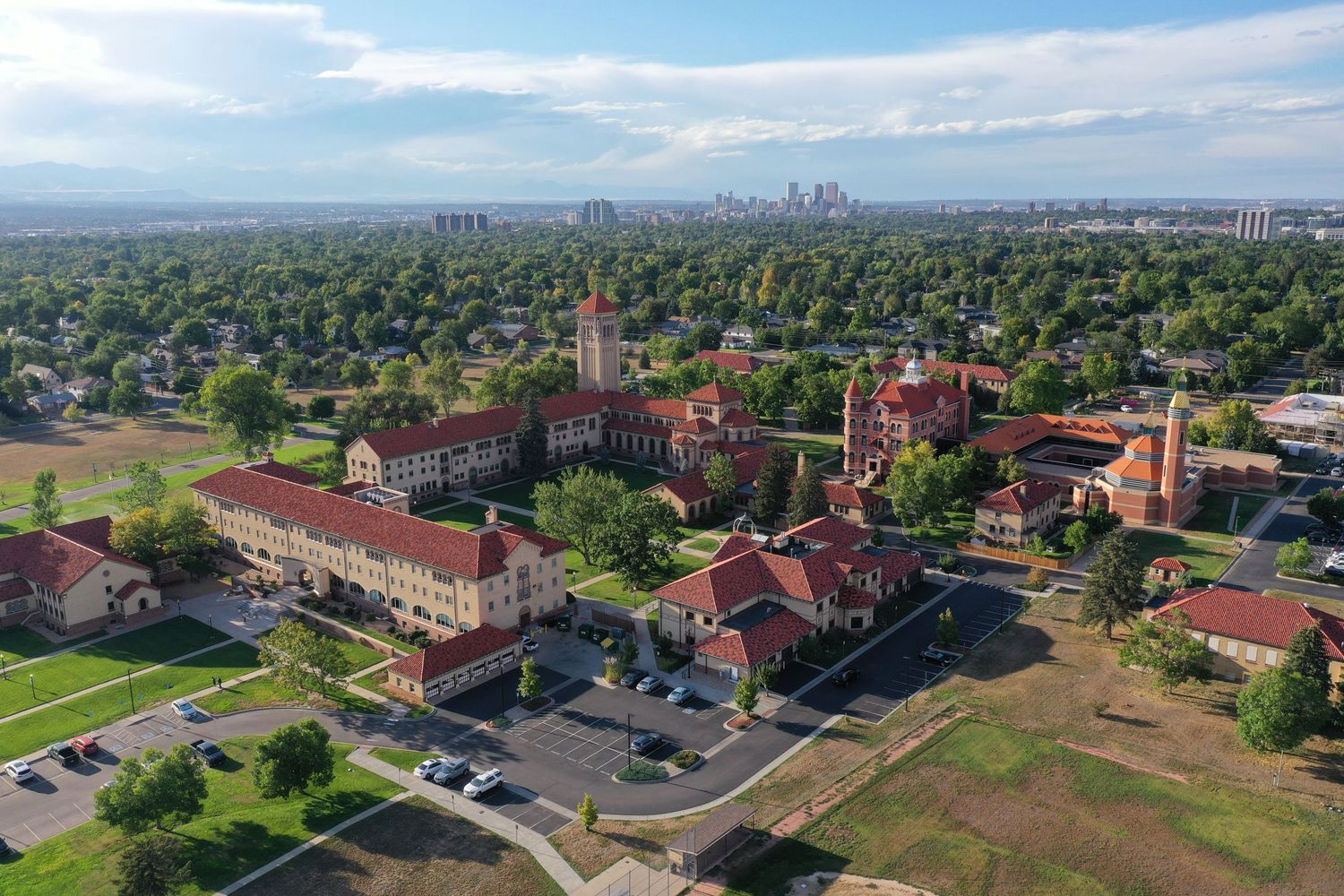 Aerial view of historic red brick buildings on a campus with Denver skyline visible in the background.