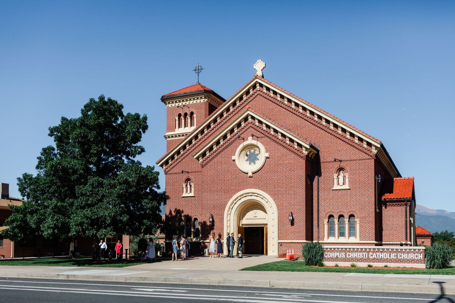 Red brick church buildings with white trim and steeples stand against a bright blue sky.