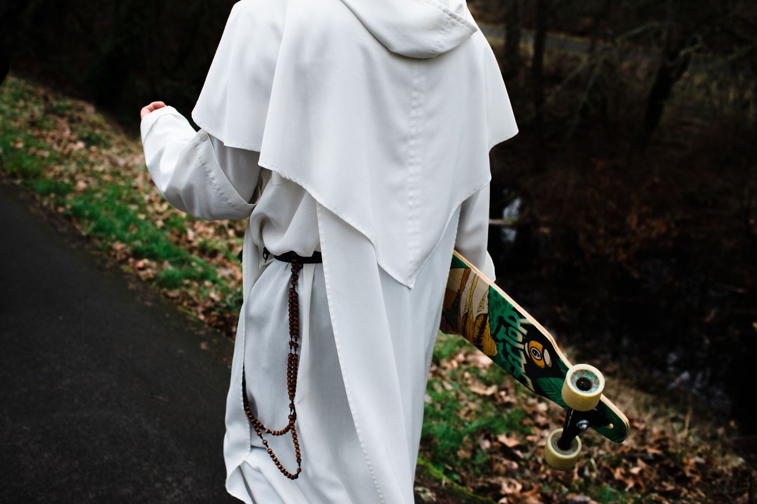 Monk in white robes holding a skateboard while walking on a path.