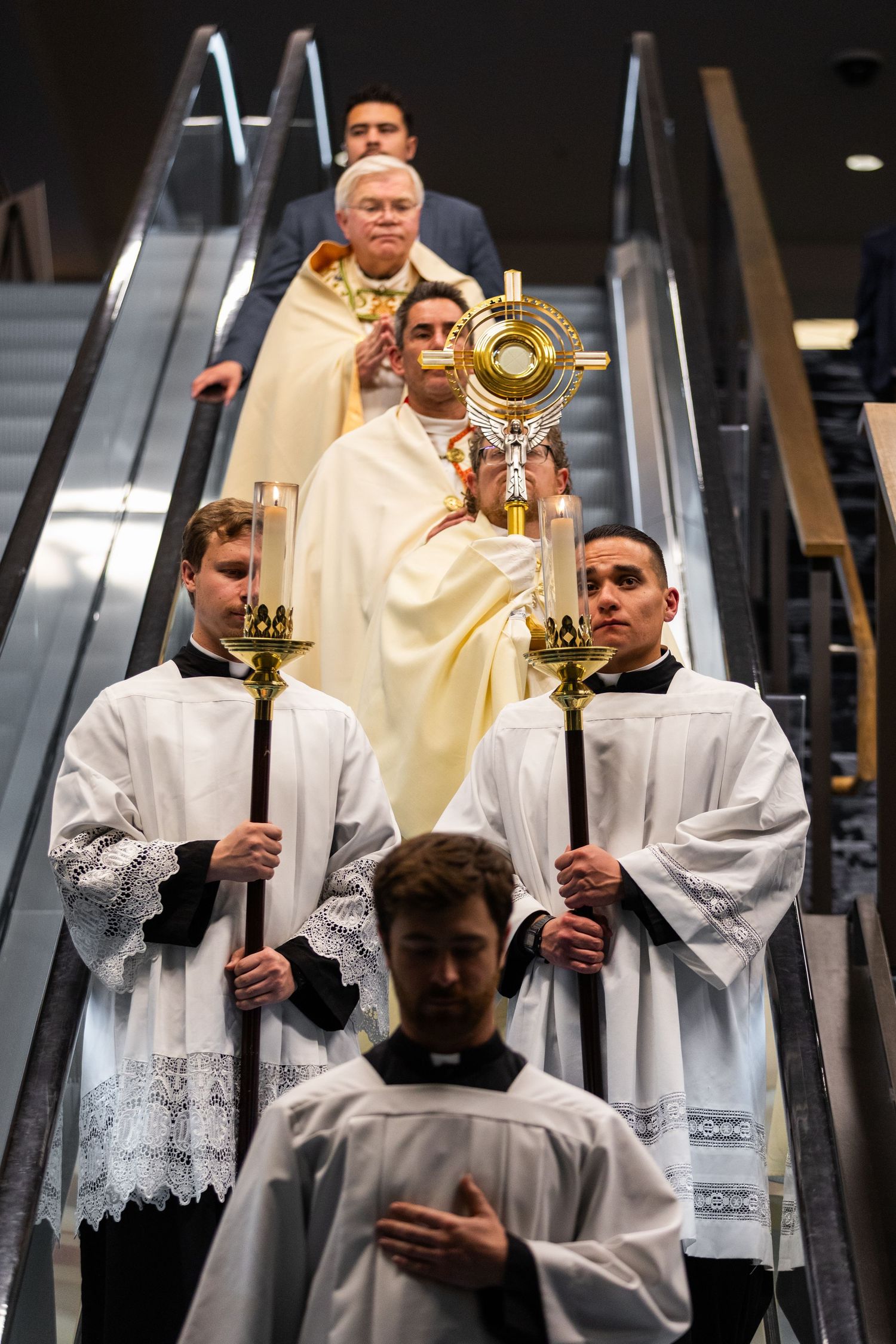 Religious procession on an escalator with clergy members holding ceremonial objects and wearing traditional robes.