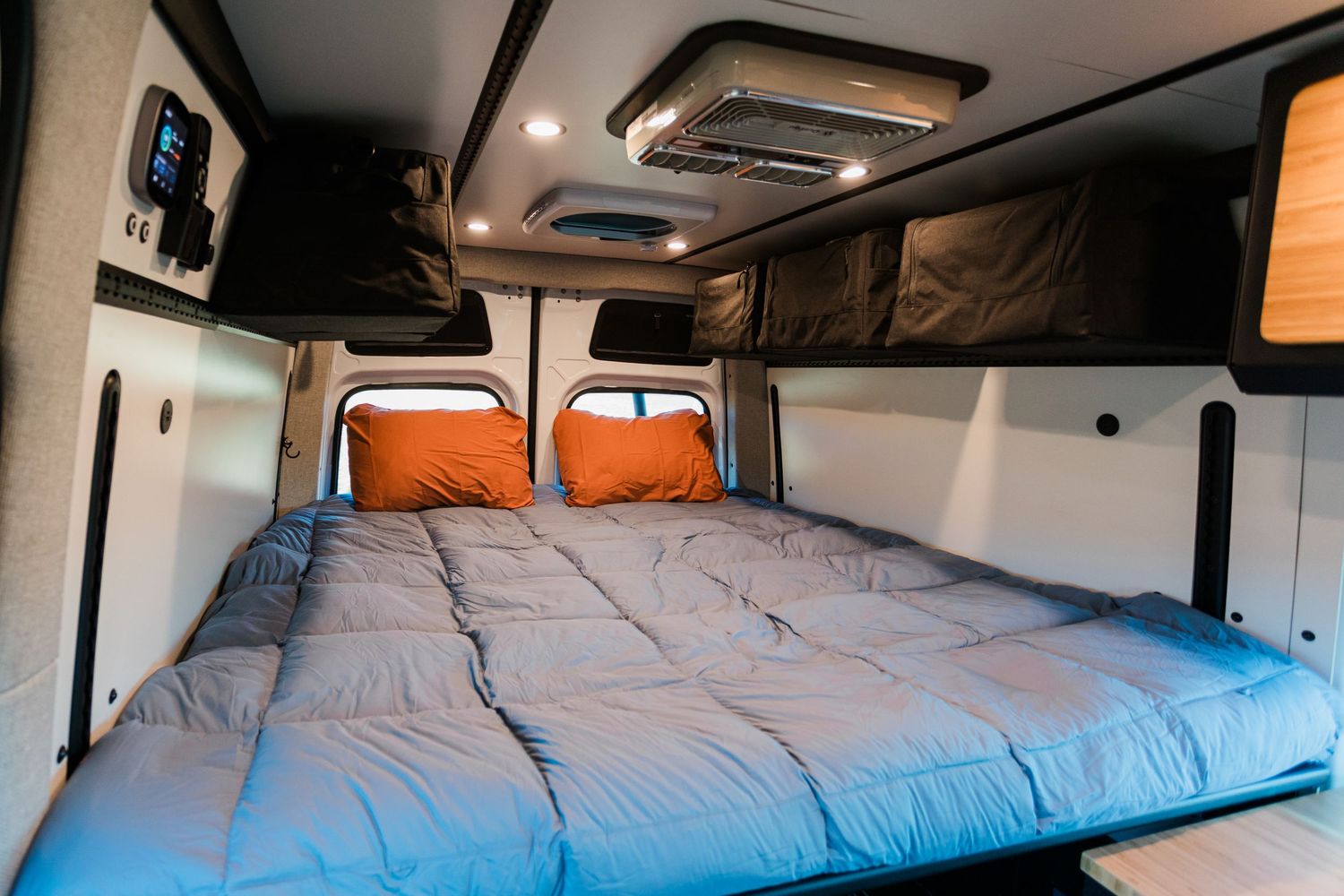 Interior view of a camper van conversion showing a comfortable bed setup with blue bedding.