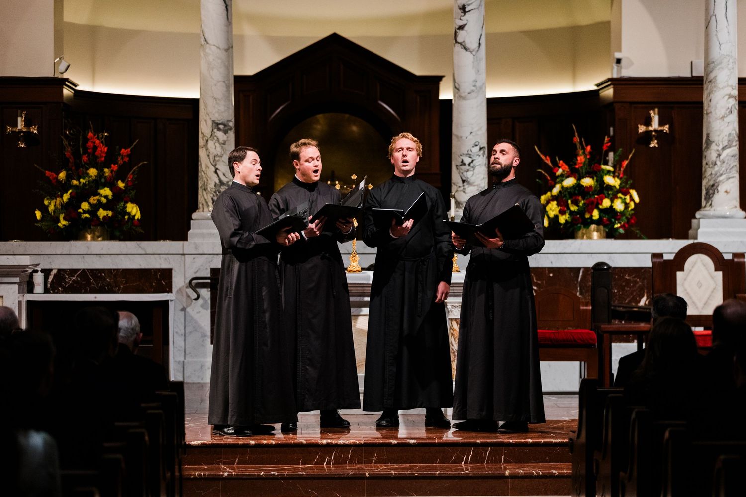 People in black attire gather at a dimly lit church altar during what appears to be a formal ceremony or service.