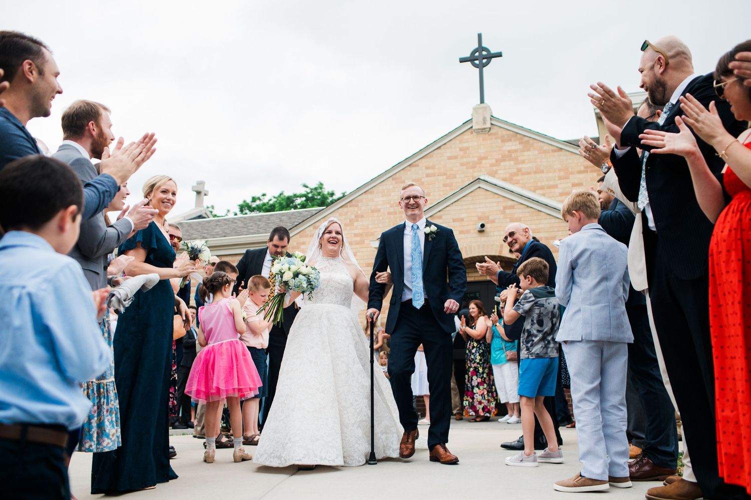 Newlyweds exit church through joyful crowd of guests clapping and celebrating their wedding recessional.