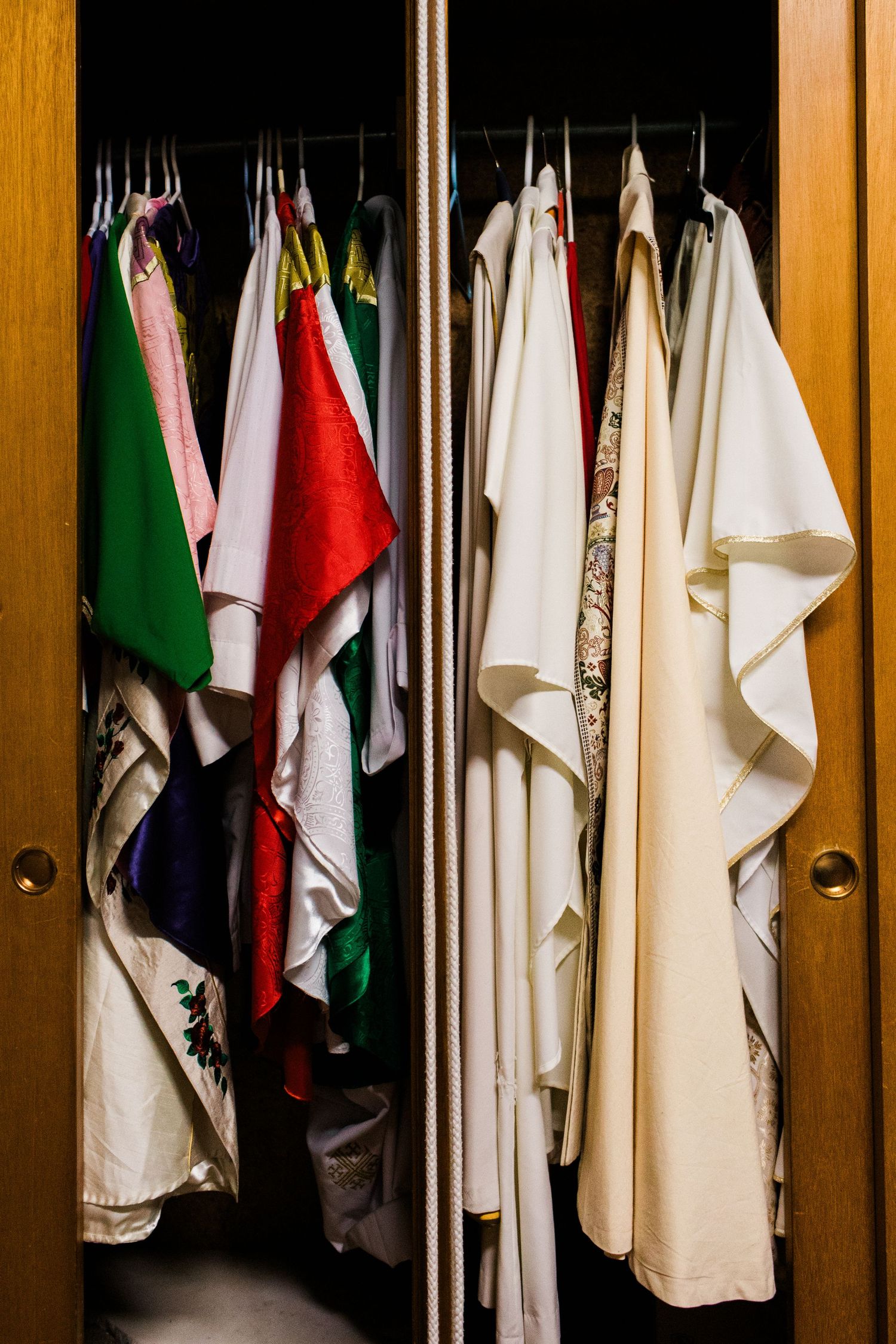 Colorful shirts and garments hanging neatly in a wooden wardrobe with warm lighting.