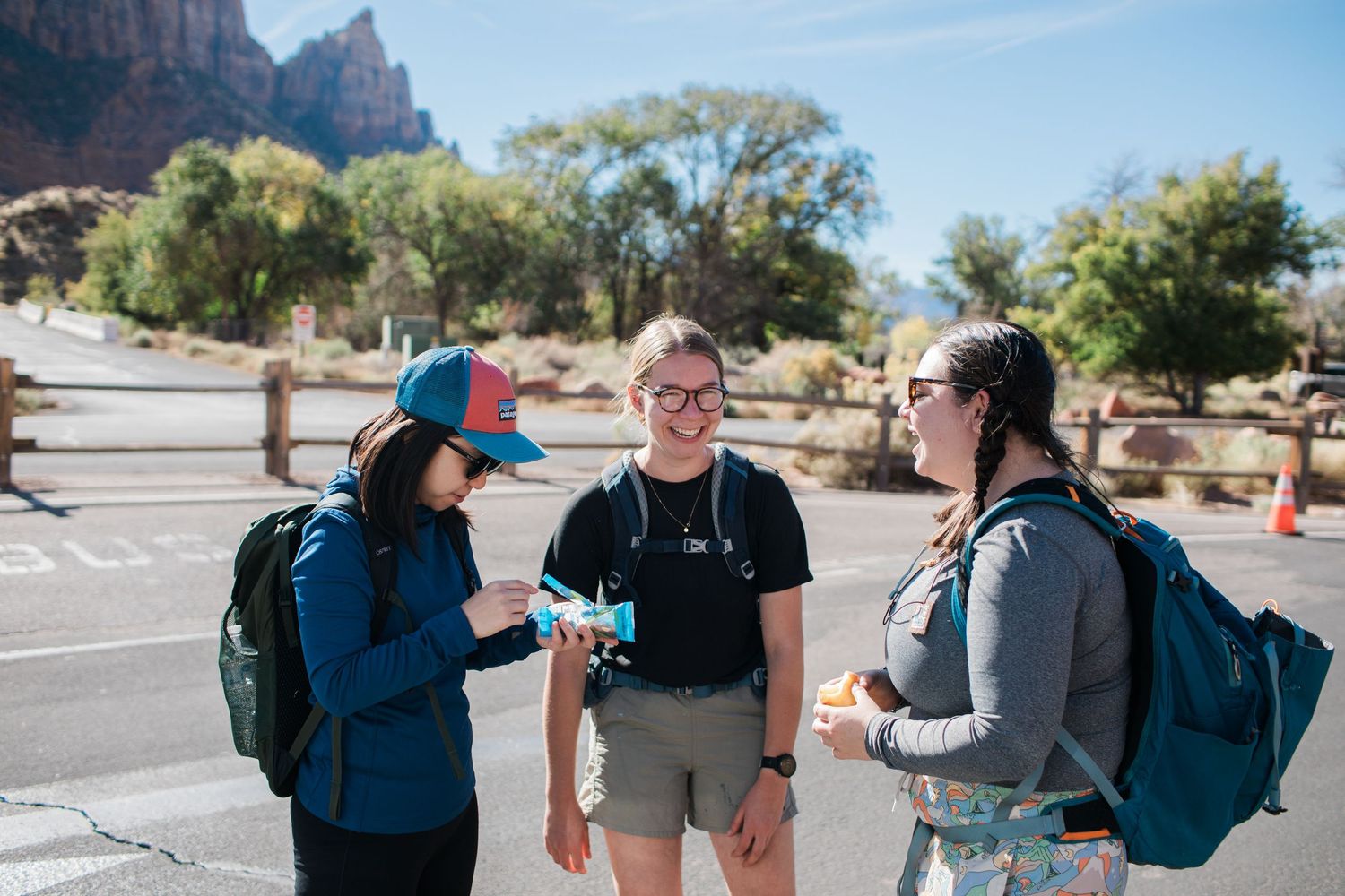 Group of hikers with backpacks gather in a sunny parking lot before starting their outdoor adventure.