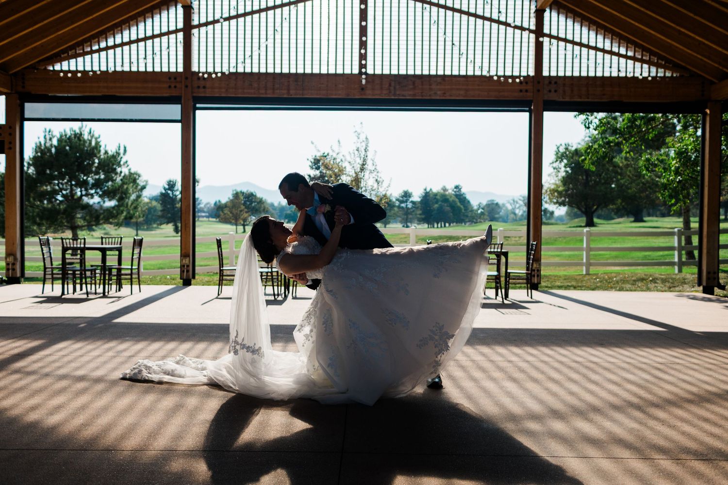 Bride and groom share a romantic dip dance inside a rustic wooden wedding venue overlooking a lush green golf course.