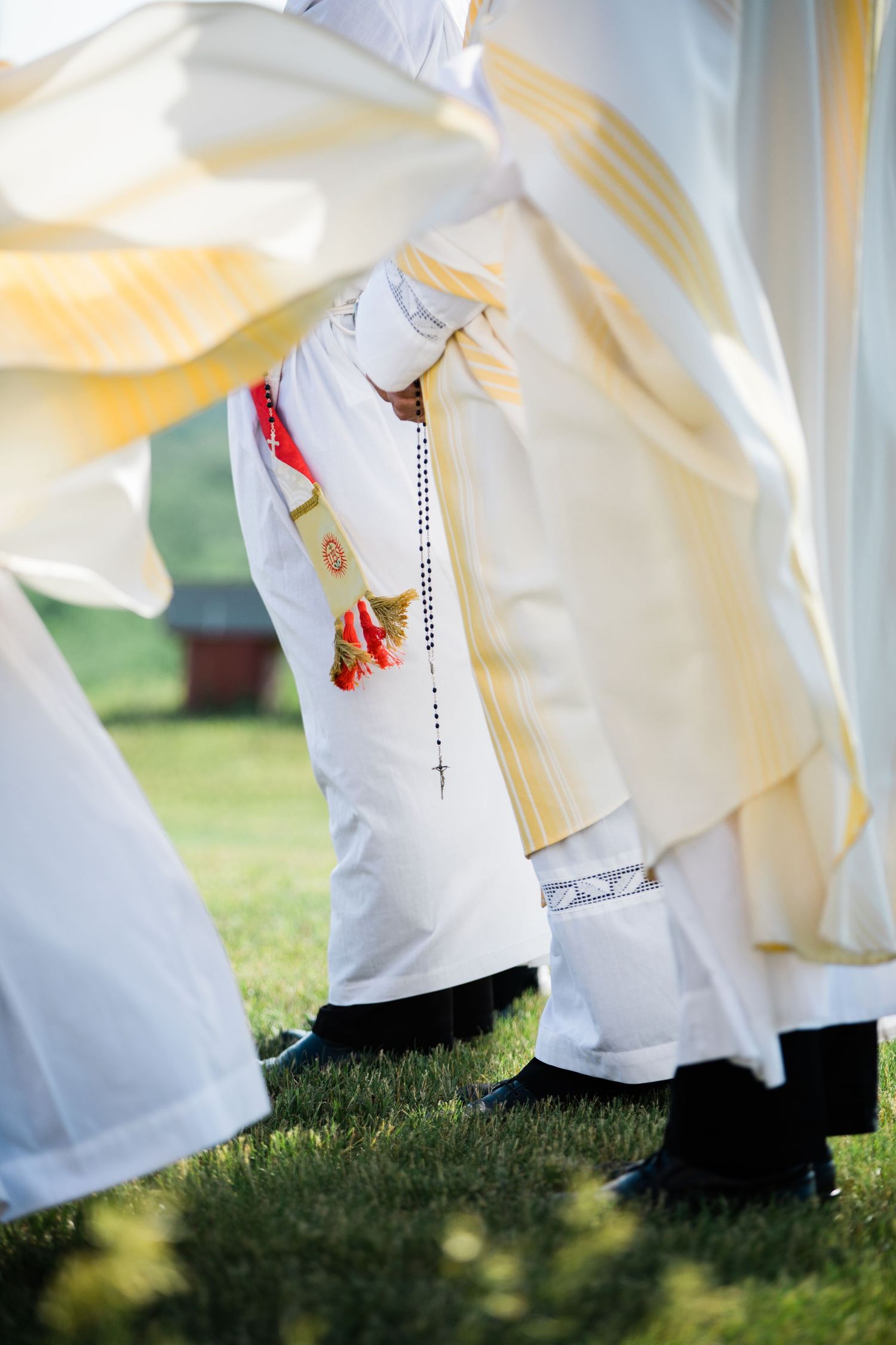 Row of white robes with glimpses of red shoes visible at ground level on grass.