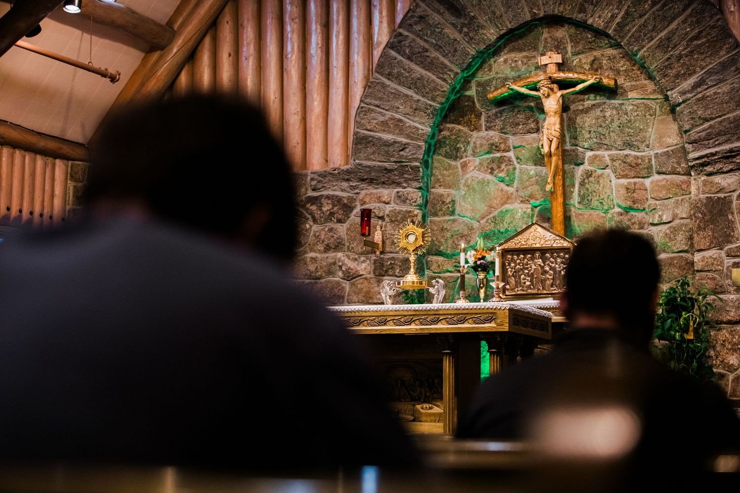 Catholic church interior with crucifix on stone altar wall during Mass service.