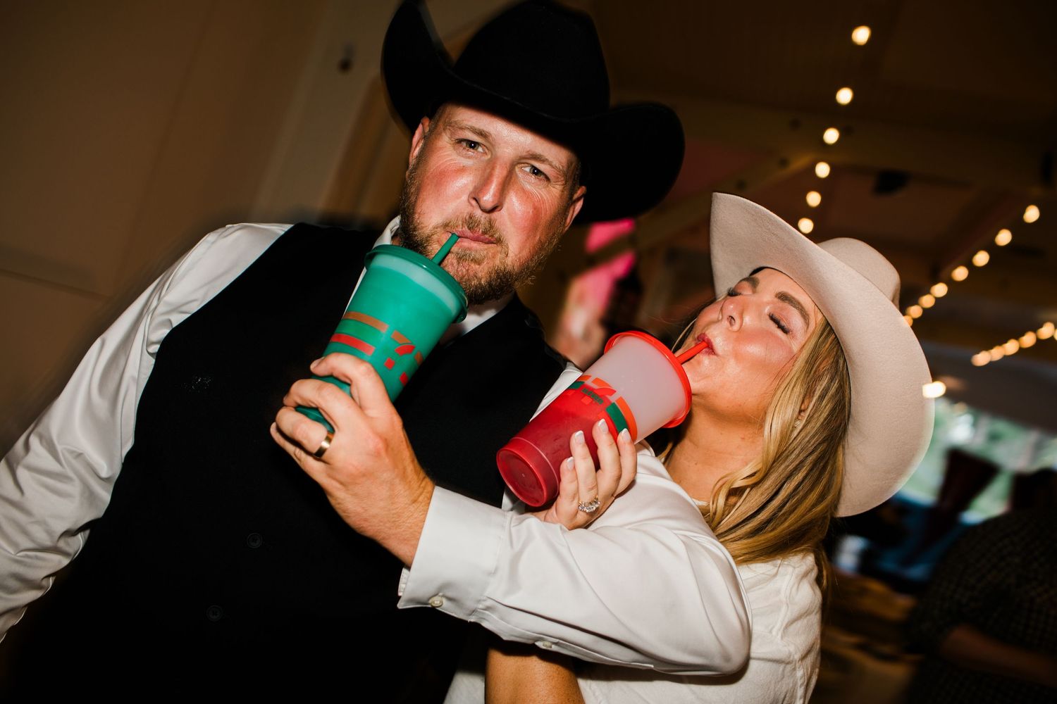 Couple in cowboy hats drinking from colorful tumblers at a country western party celebration.