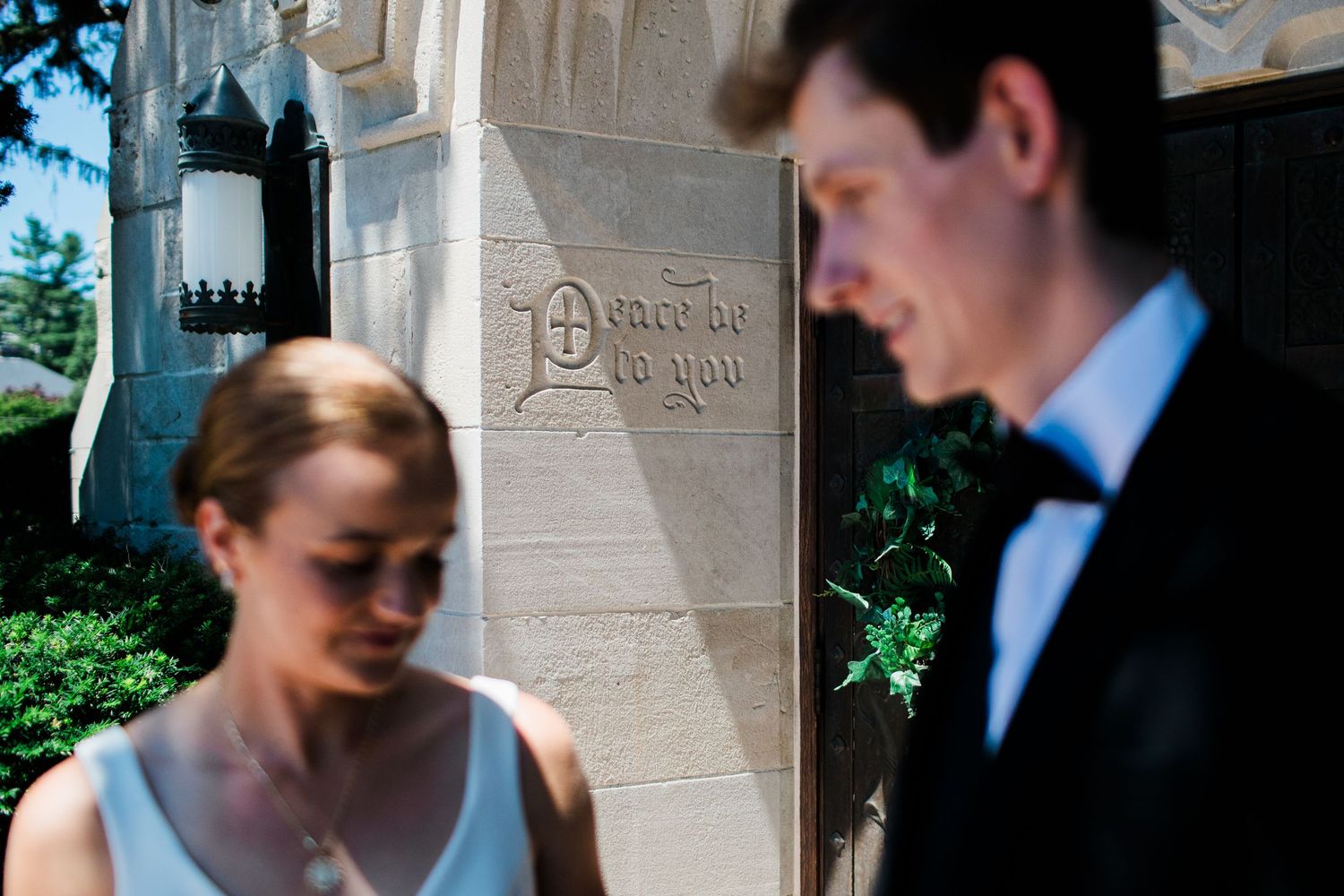 Bride and groom in formal attire stand outside an ornate stone building with decorative carved signage.