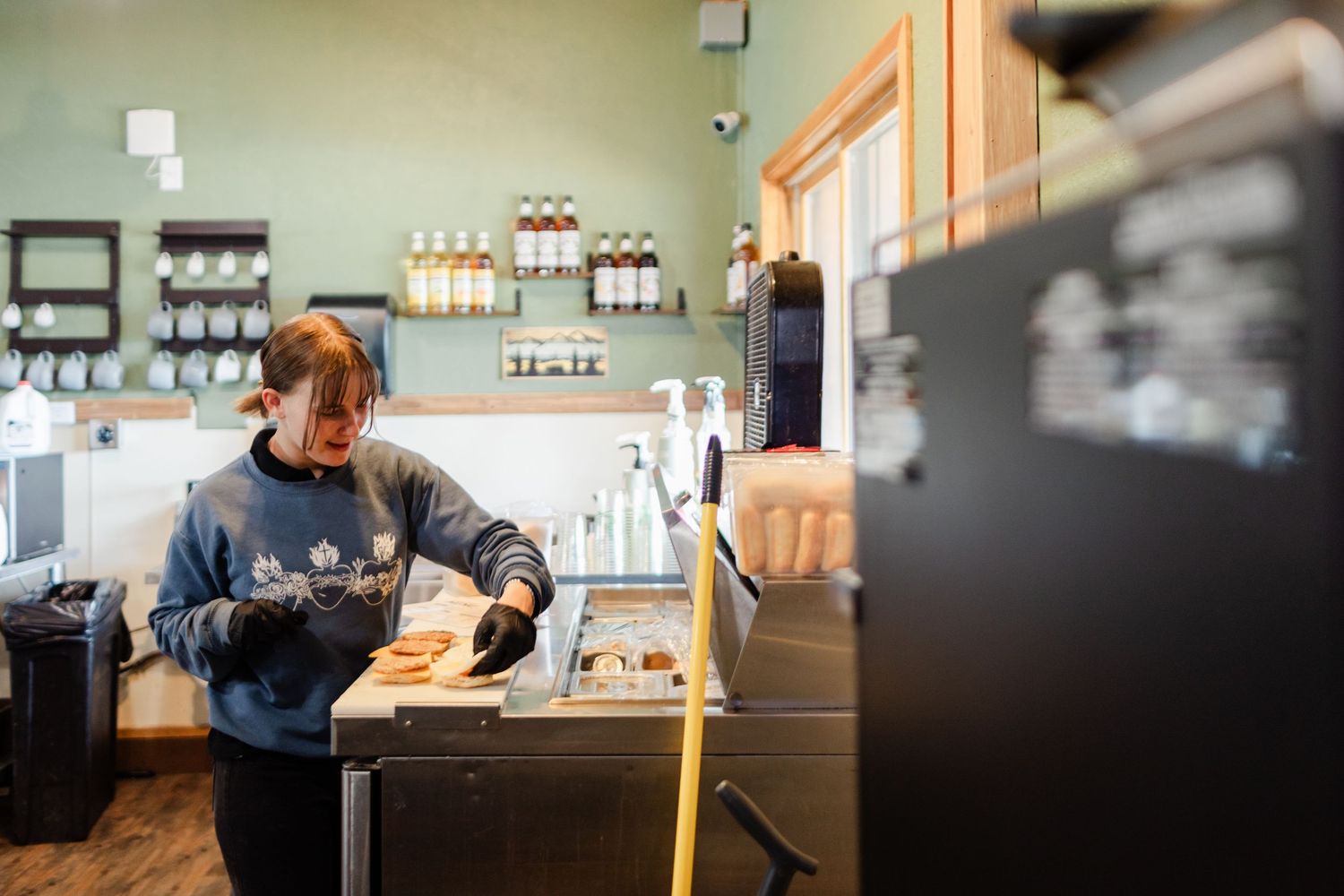 Barista preparing coffee drinks at a modern cafe counter with wood accents and natural lighting.