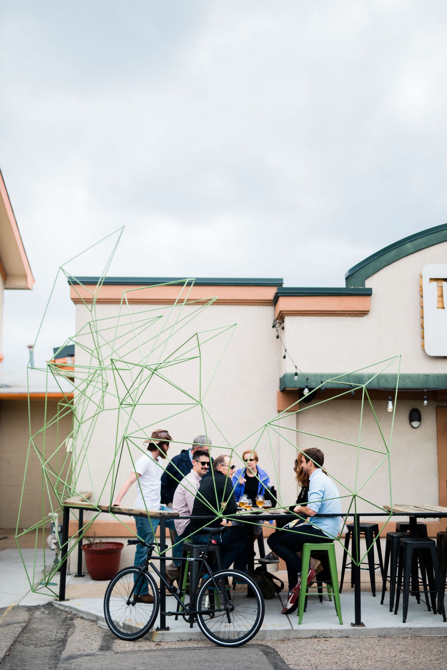 People gathered at an outdoor brewery patio with tables, chairs and bicycles parked nearby.