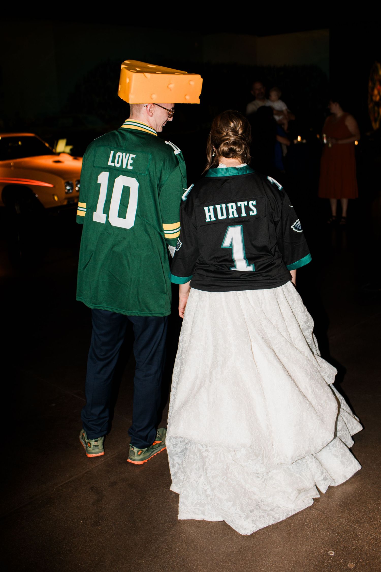 Bride and groom wear NFL jerseys at wedding, she in Eagles Hurts #1, he in Packers Love #10 with cheesehead hat.