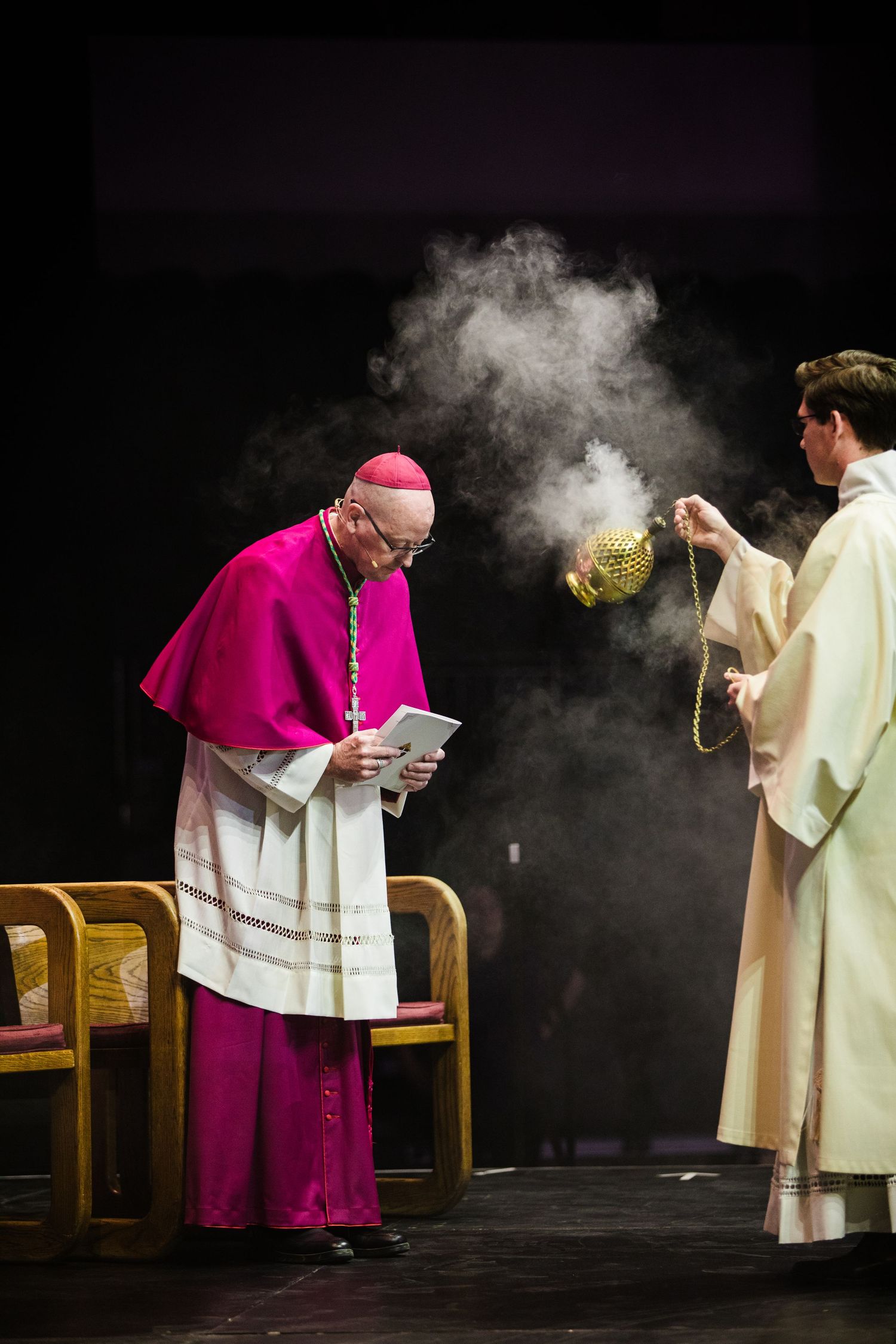 Two figures in religious ceremonial attire perform a ritual with incense smoke during a sacred service.
