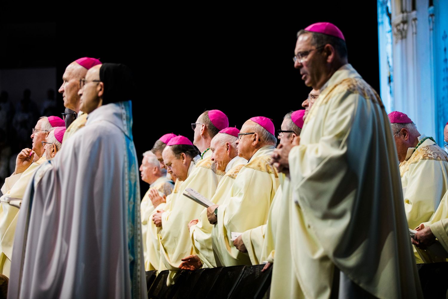 Group of clergy members in ceremonial robes and pink zuchettos gathered during formal church service.