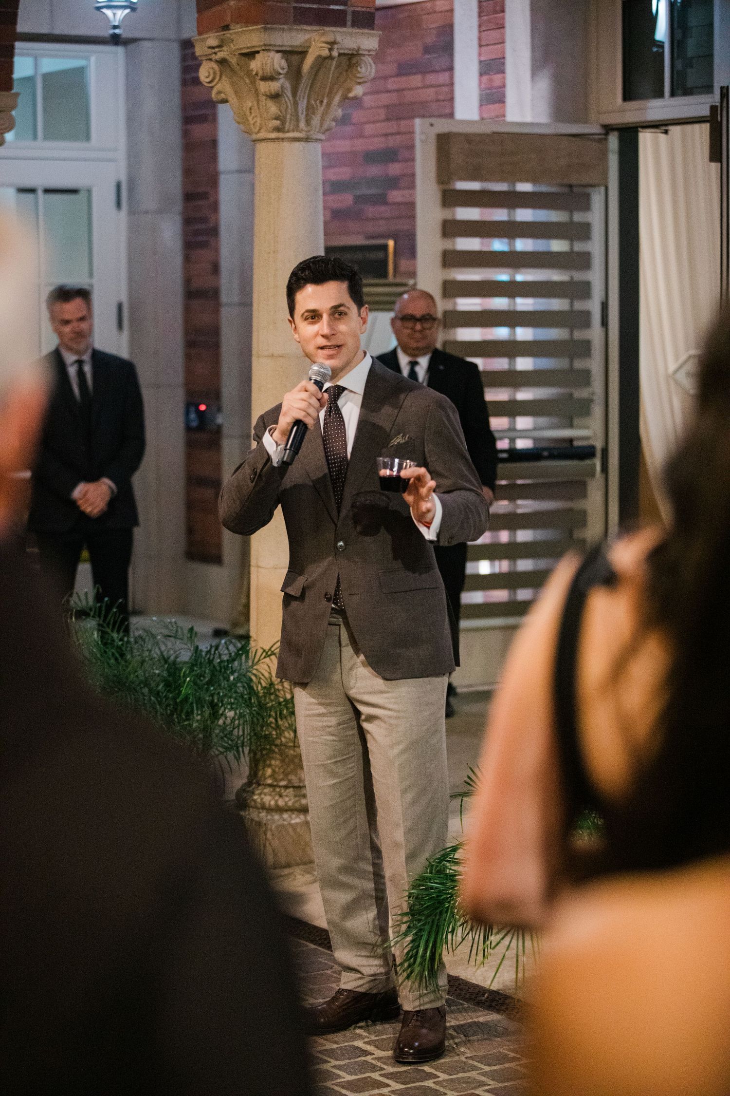 A person in business attire walks across a room with brick walls and decorative columns.