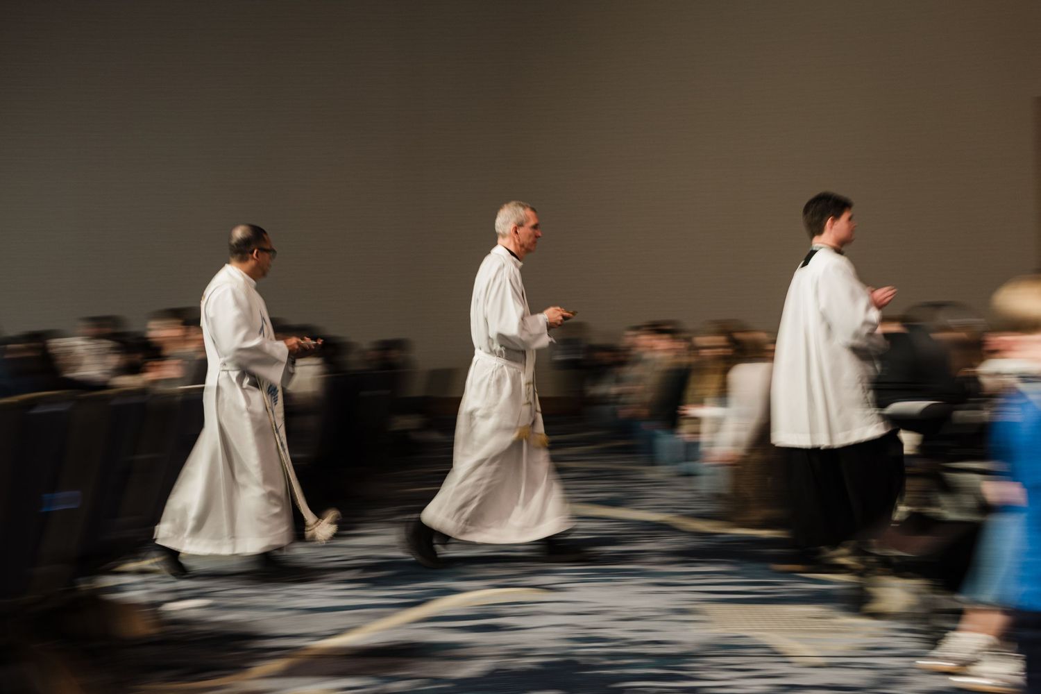 Artistic motion blur photograph shows people in white clothing moving across a dark floor in a sequential pattern.